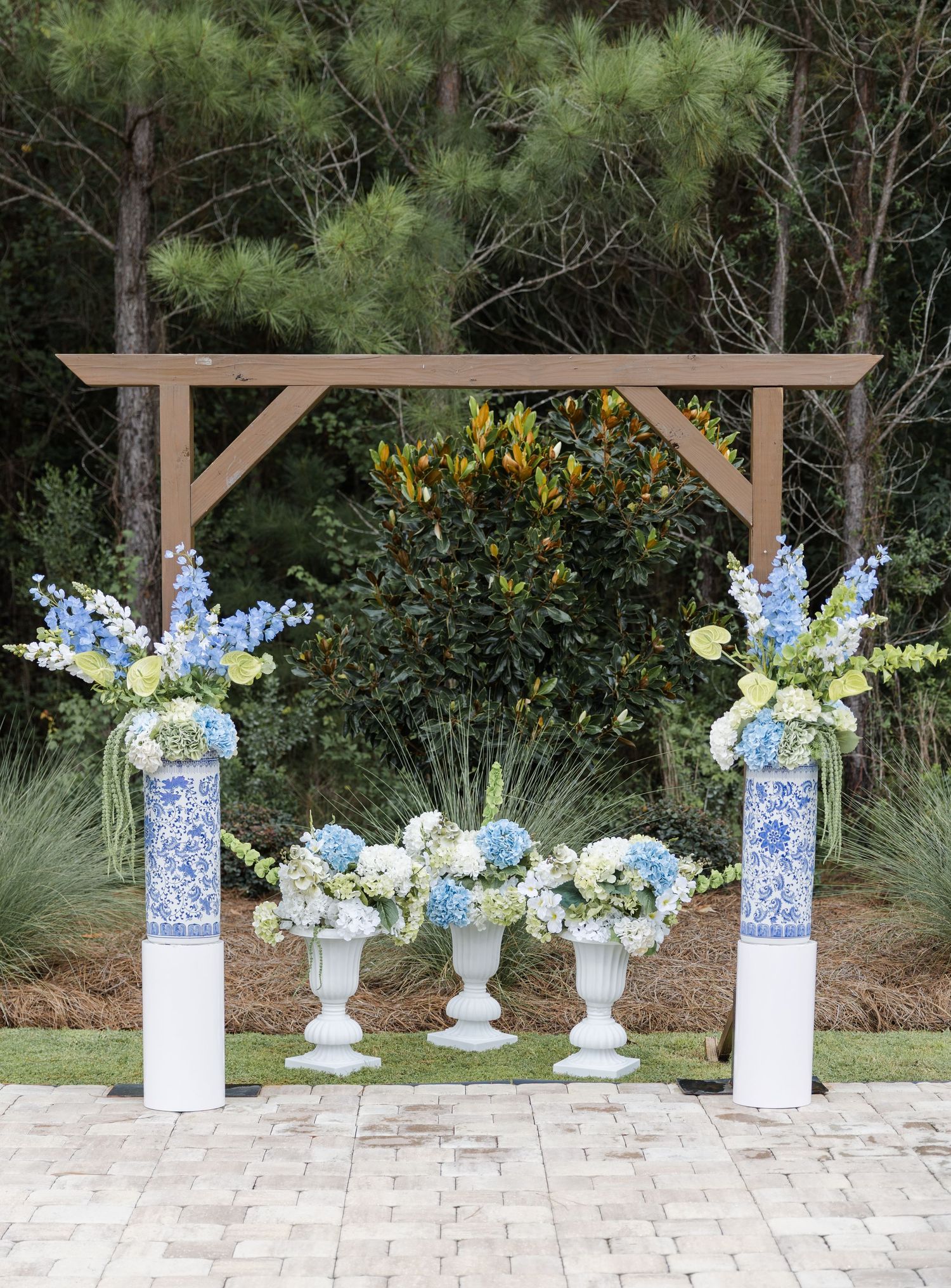 Outdoor wedding ceremony arch with blue hydrangea and white floral arrangements in blue chinoiserie vases.