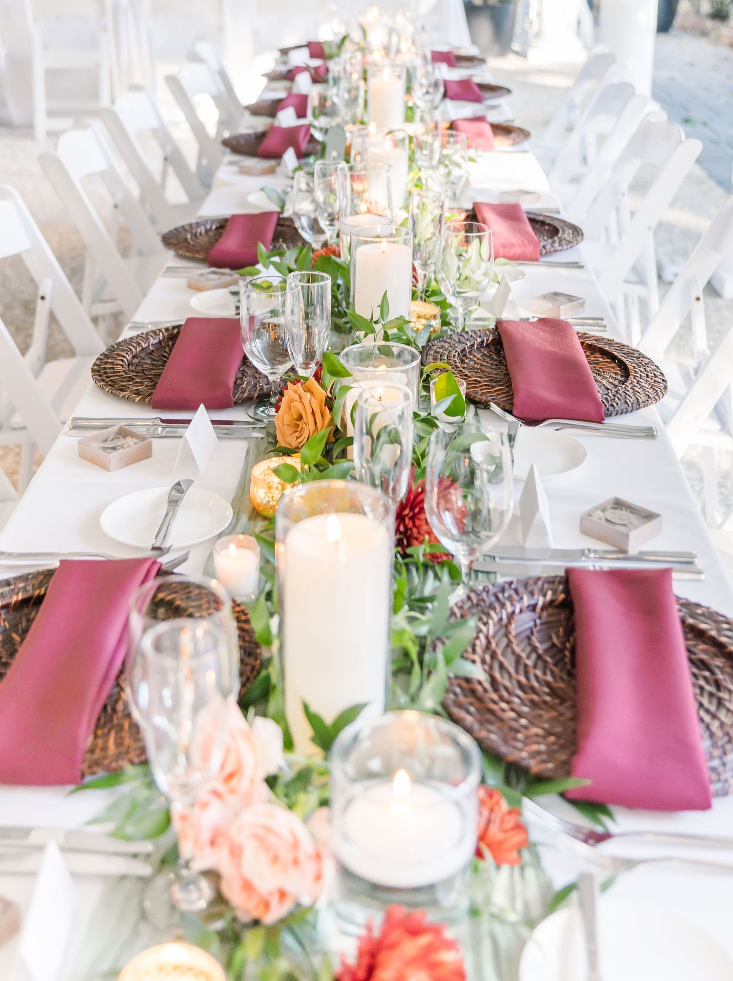 Elegant wedding reception table setting with pink napkins, woven chargers, and coral floral centerpieces.