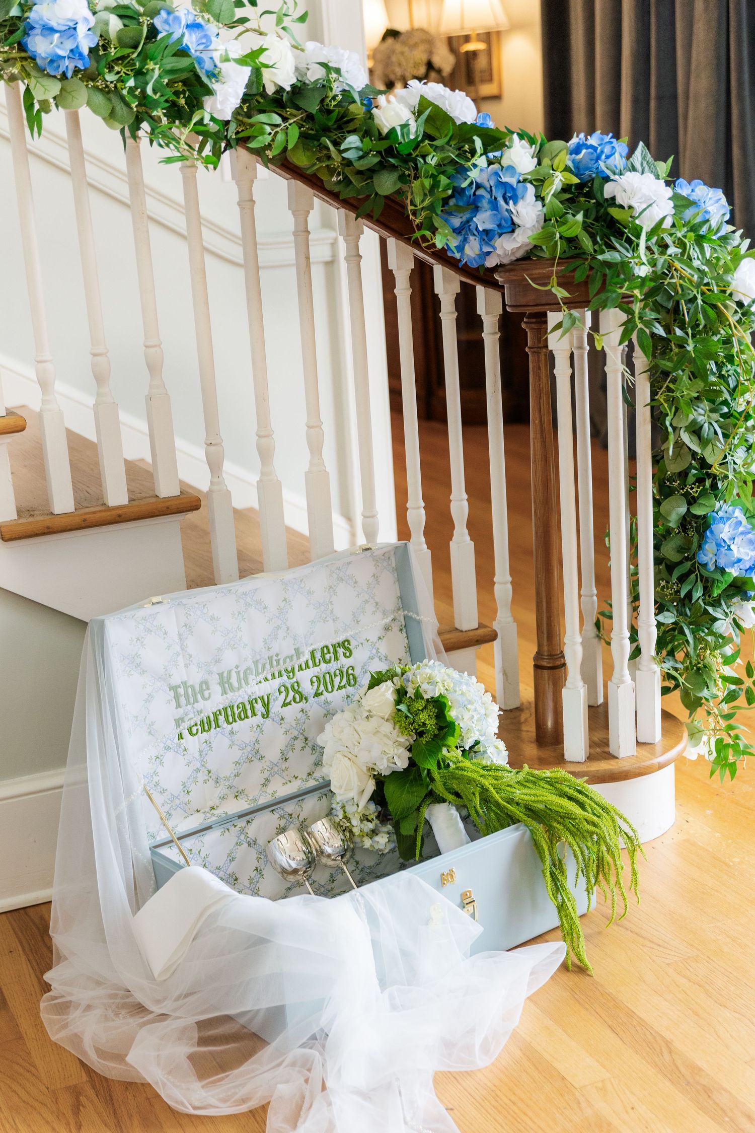 Wedding staircase decorated with blue and white hydrangeas, greenery garland, and a personalized Kichlighters February 28 2026 sign.