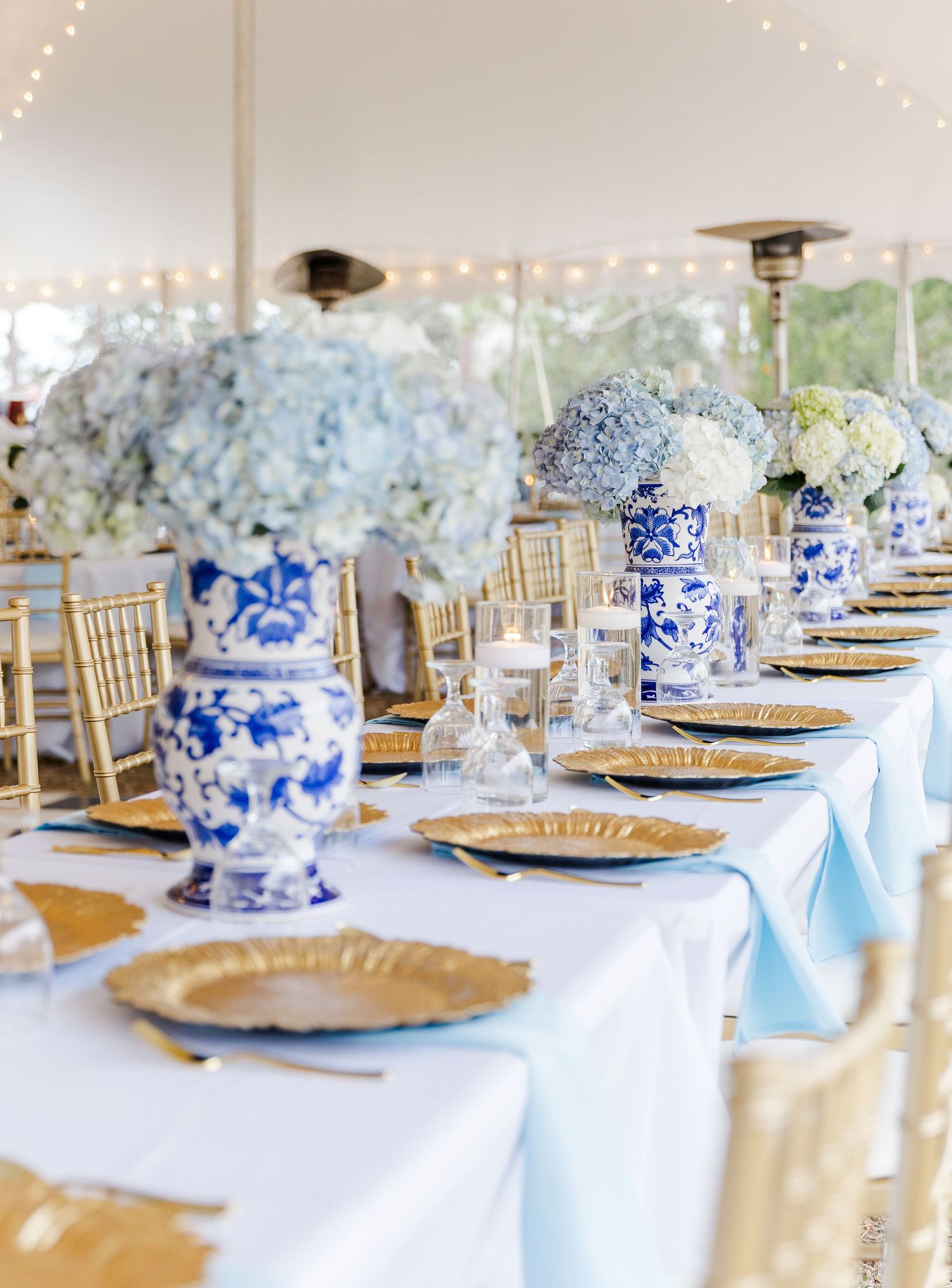 Elegant reception table with blue and white chinoiserie vases, blue hydrangeas, and gold chargers.