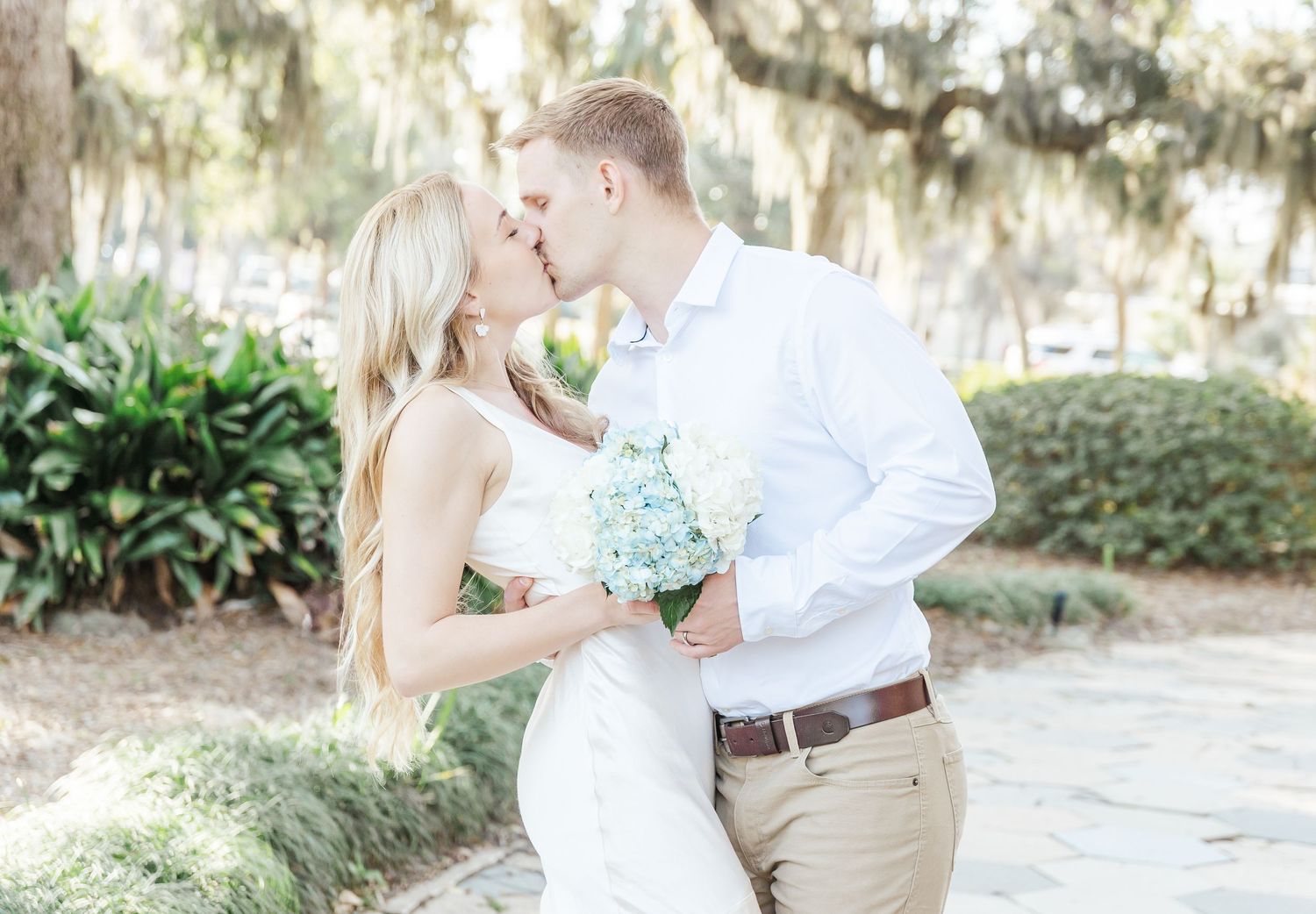 A romantic kiss shared between a couple holding blue hydrangeas in a garden setting.