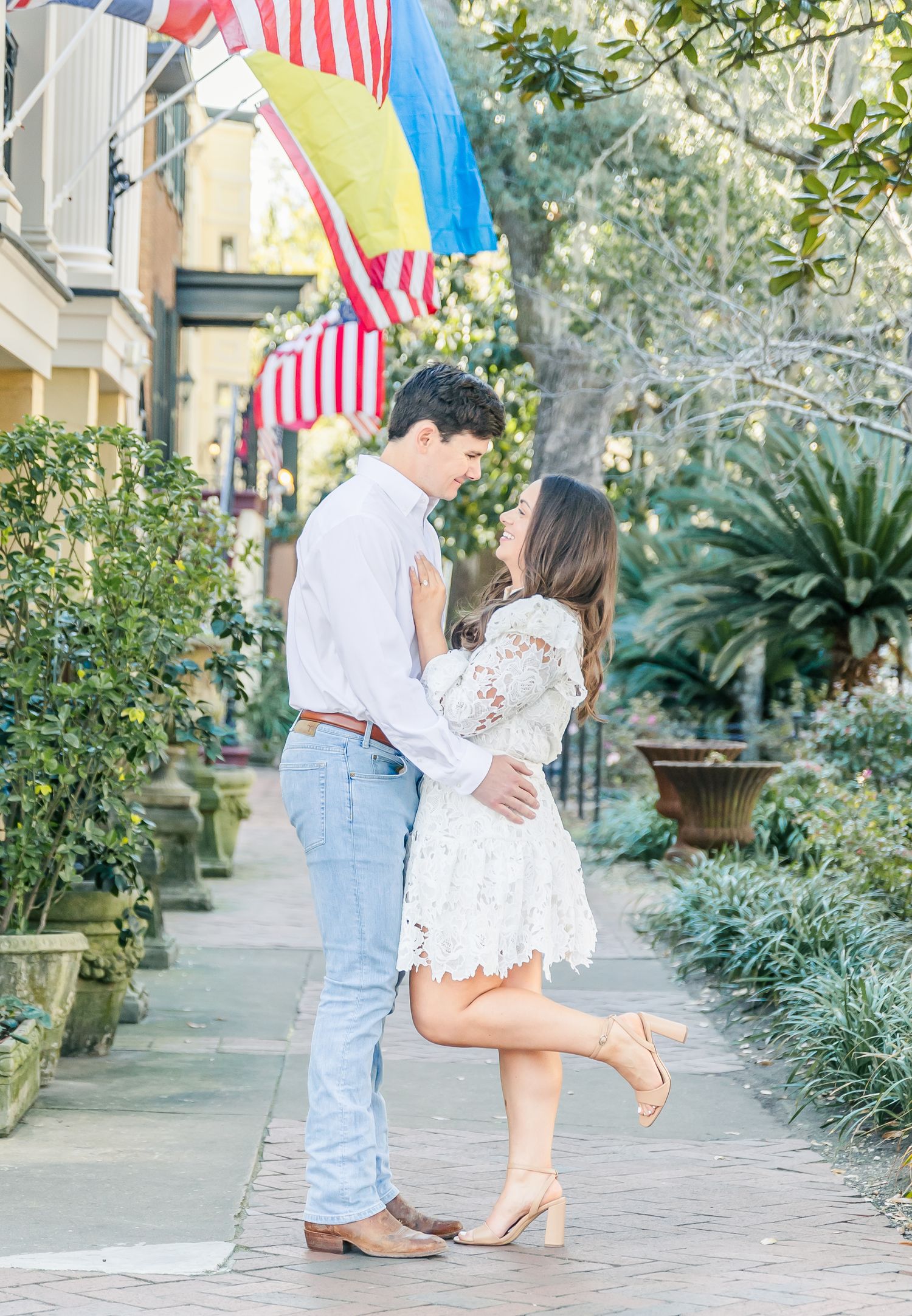 Romantic couple in light summer attire sharing tender moment under American flags.