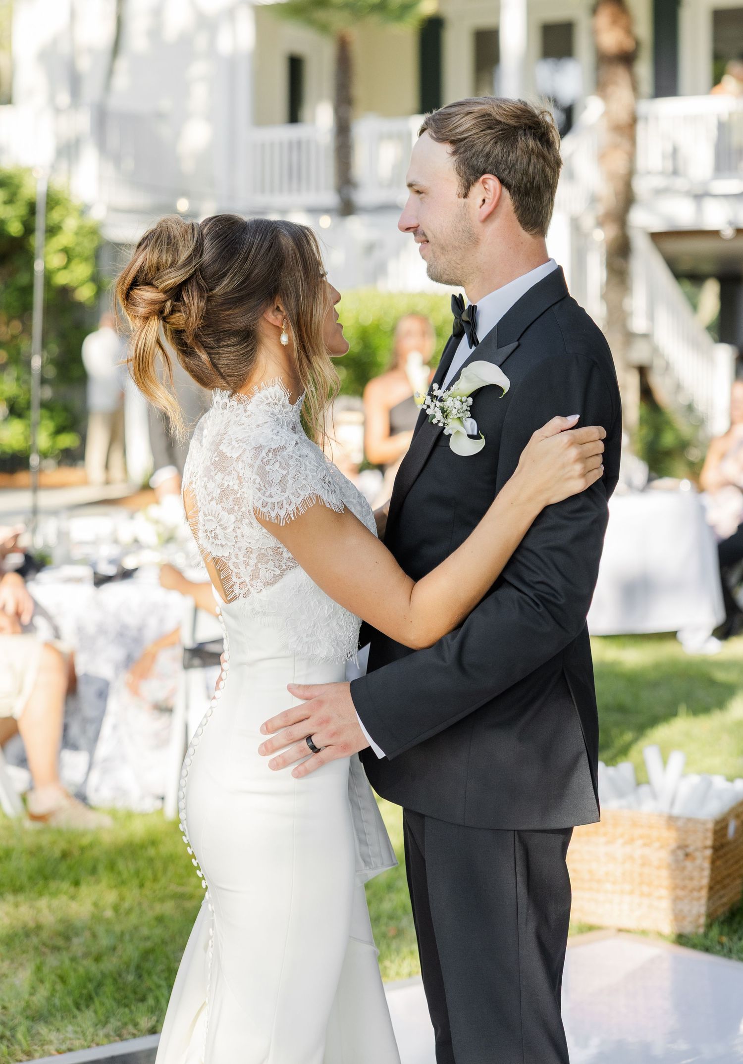 Bride and groom share their first dance outdoors at an elegant wedding reception, bride in lace gown, groom in black tuxedo.