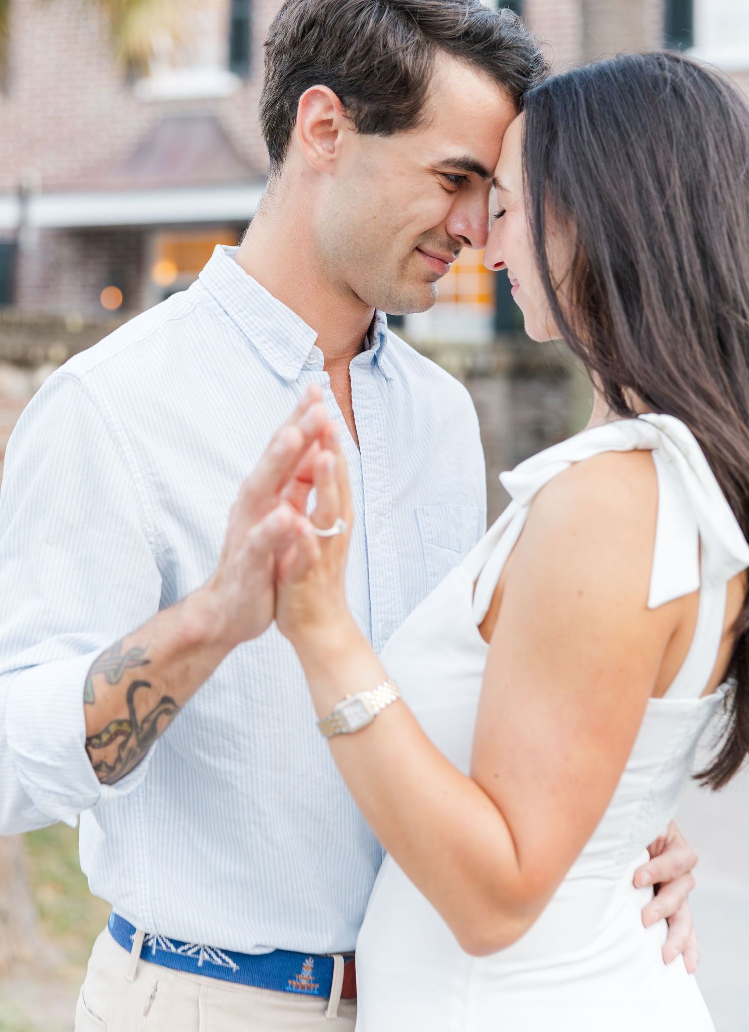 Close romantic moment of a couple touching foreheads and holding hands, man with tattoo visible on arm.