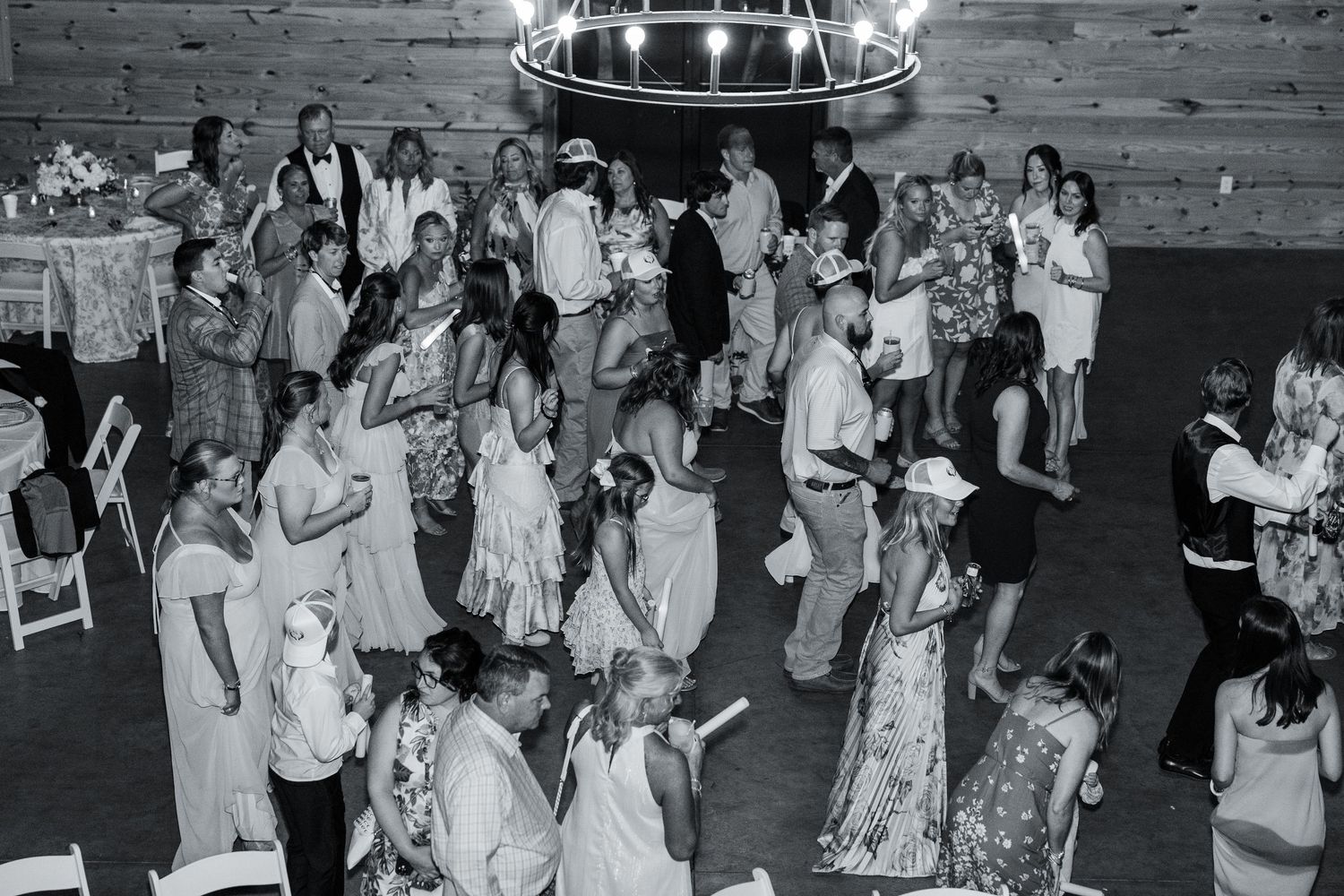 Black and white aerial view of wedding guests dancing at lively barn reception celebration.