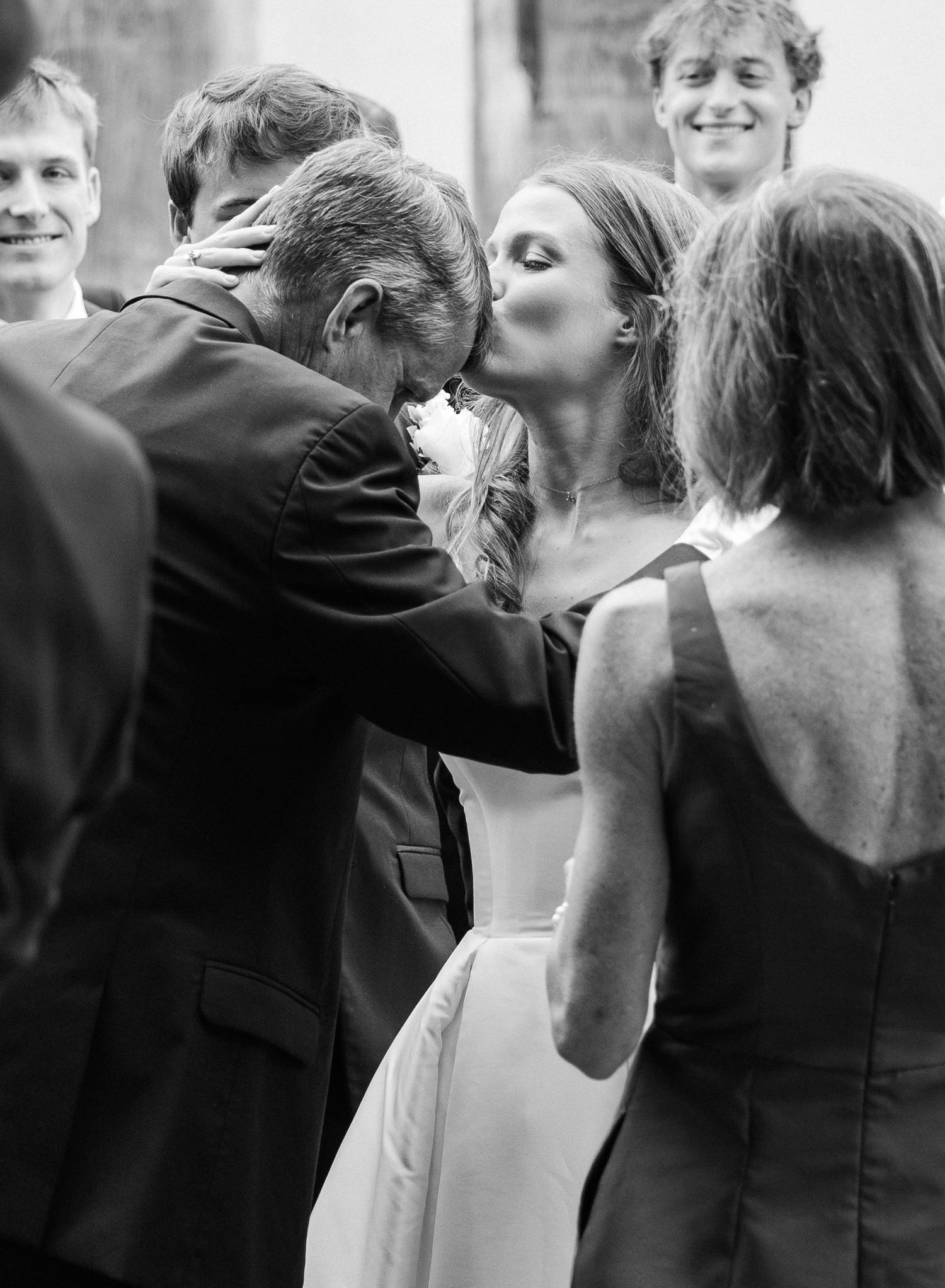 Black and white photo of bride kissing older gentleman on cheek after wedding ceremony.