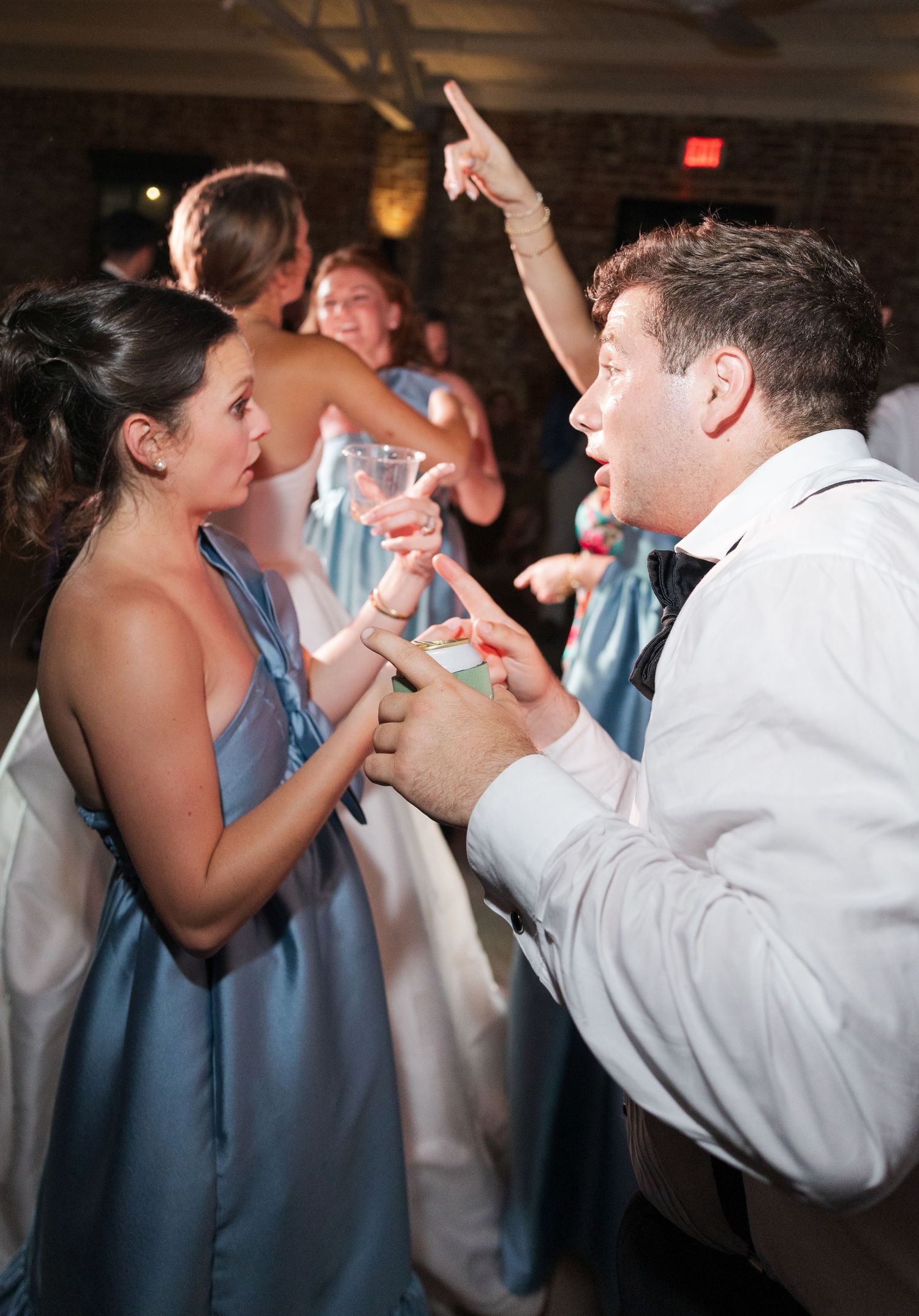 Bridesmaid in blue dress and groomsman dance energetically together at lively wedding reception.