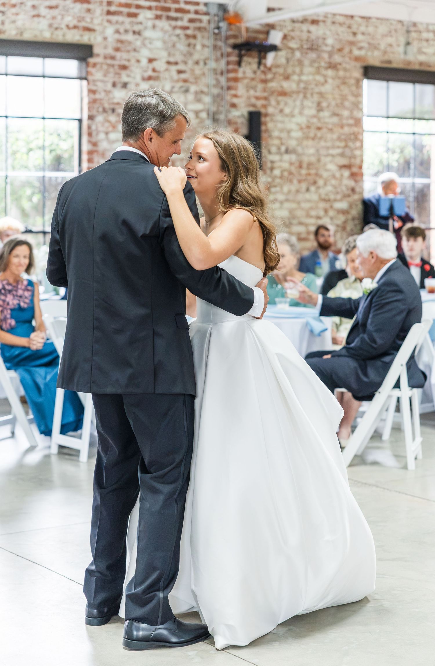 Bride and father share emotional father-daughter dance at rustic brick wedding venue.