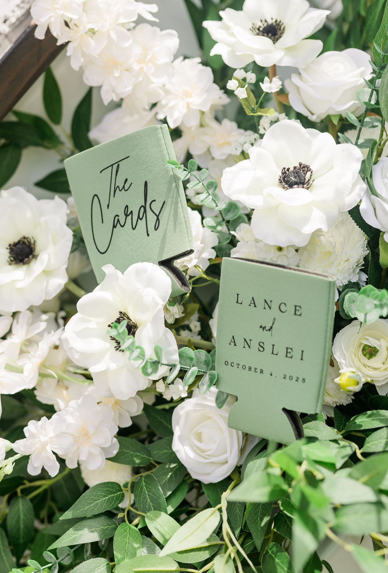 White anemones and roses with sage green place cards displayed among fresh greenery.