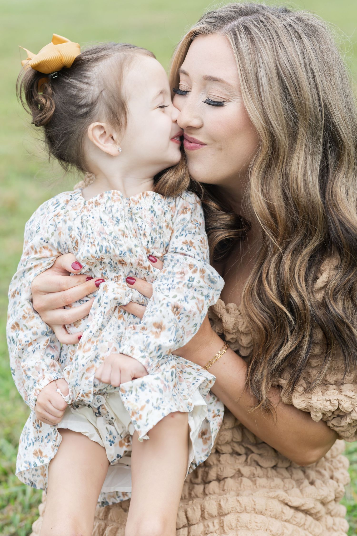 A tender moment shared between parent and child in a floral dress against a green outdoor backdrop.