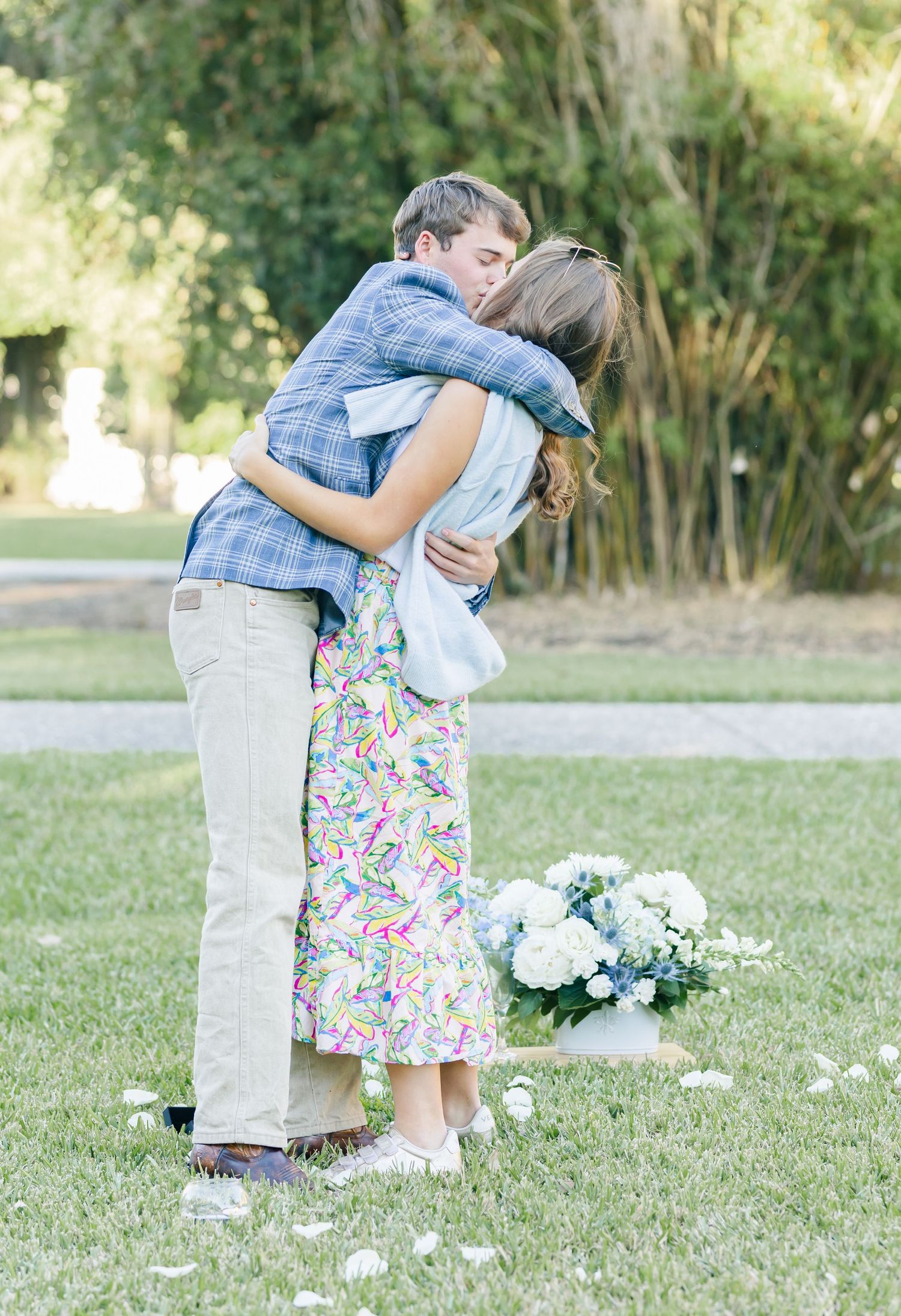 A tender embrace captured outdoors with white floral arrangements on the ground.