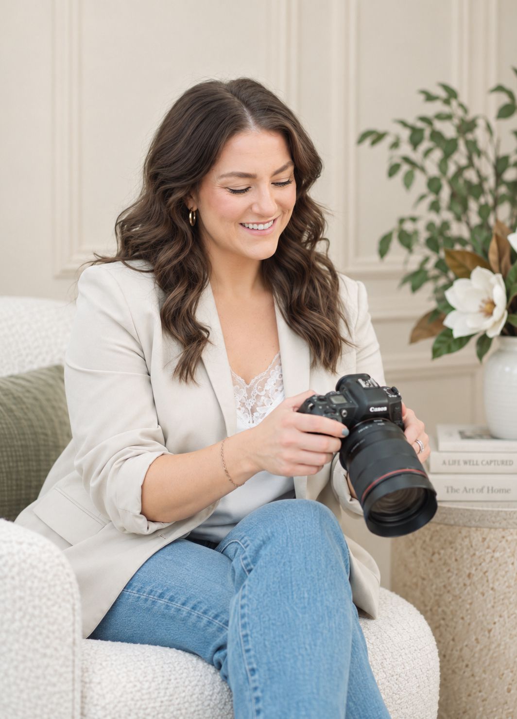 Smiling woman in beige blazer reviewing photos on Canon DSLR camera while seated in white chair.