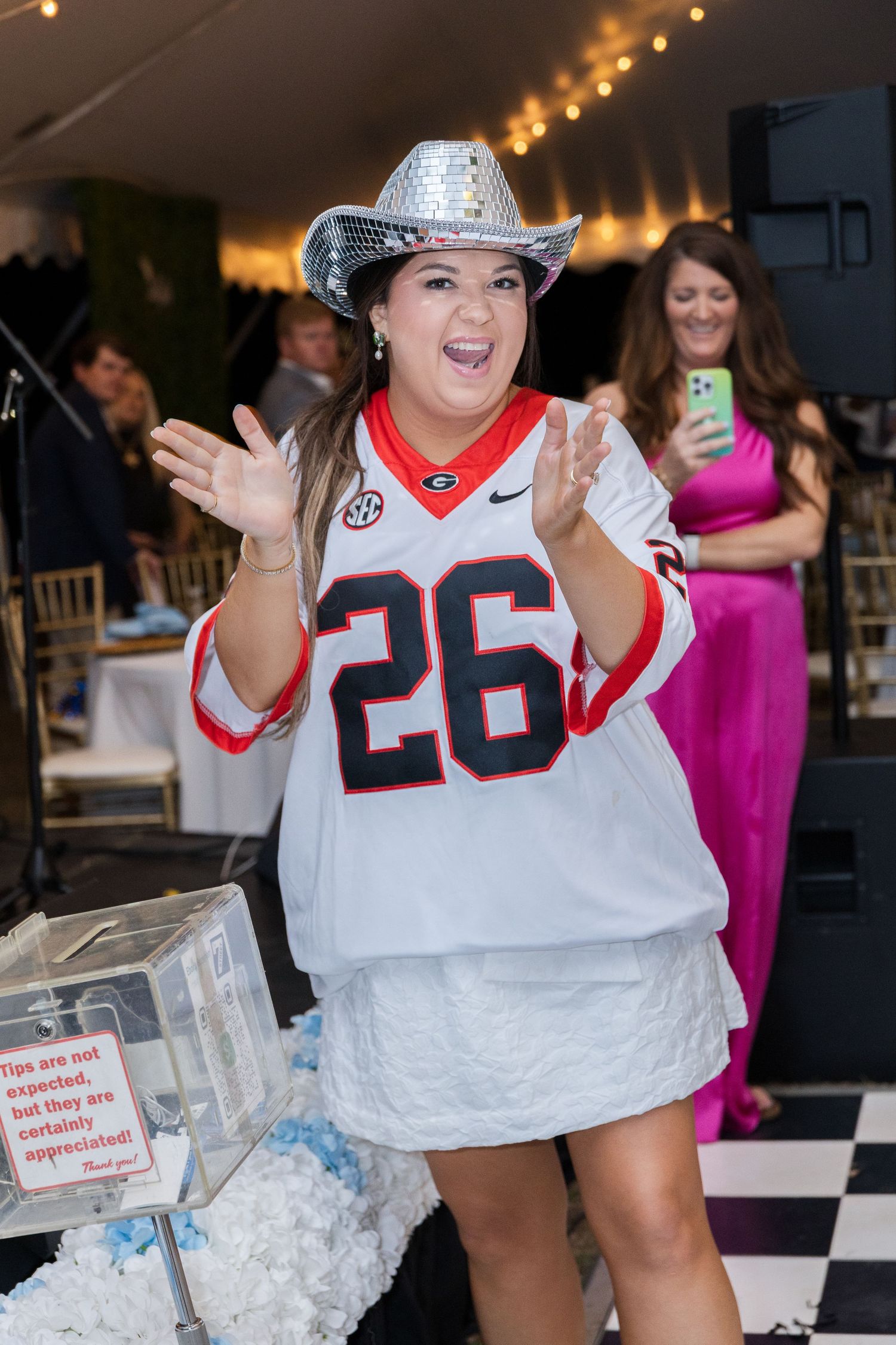Bride wearing Georgia Bulldogs jersey and sequin cowboy hat celebrating at wedding reception.