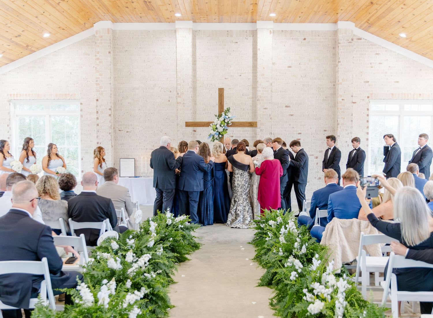 Wedding guests and bridal party gather in prayer around the couple at the altar during ceremony.