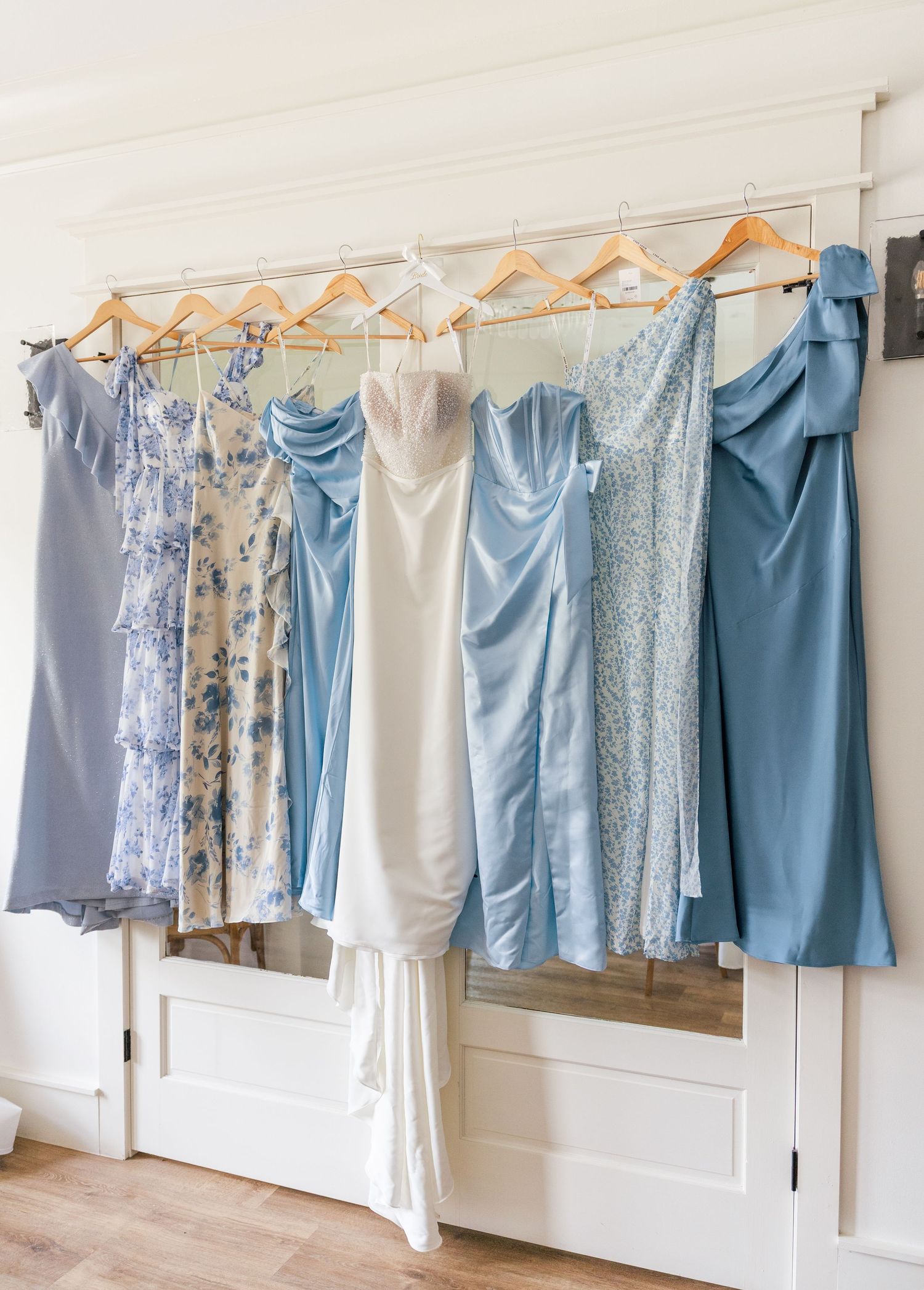 Blue and white bridesmaid dresses hanging on a rack beside a white wedding gown.