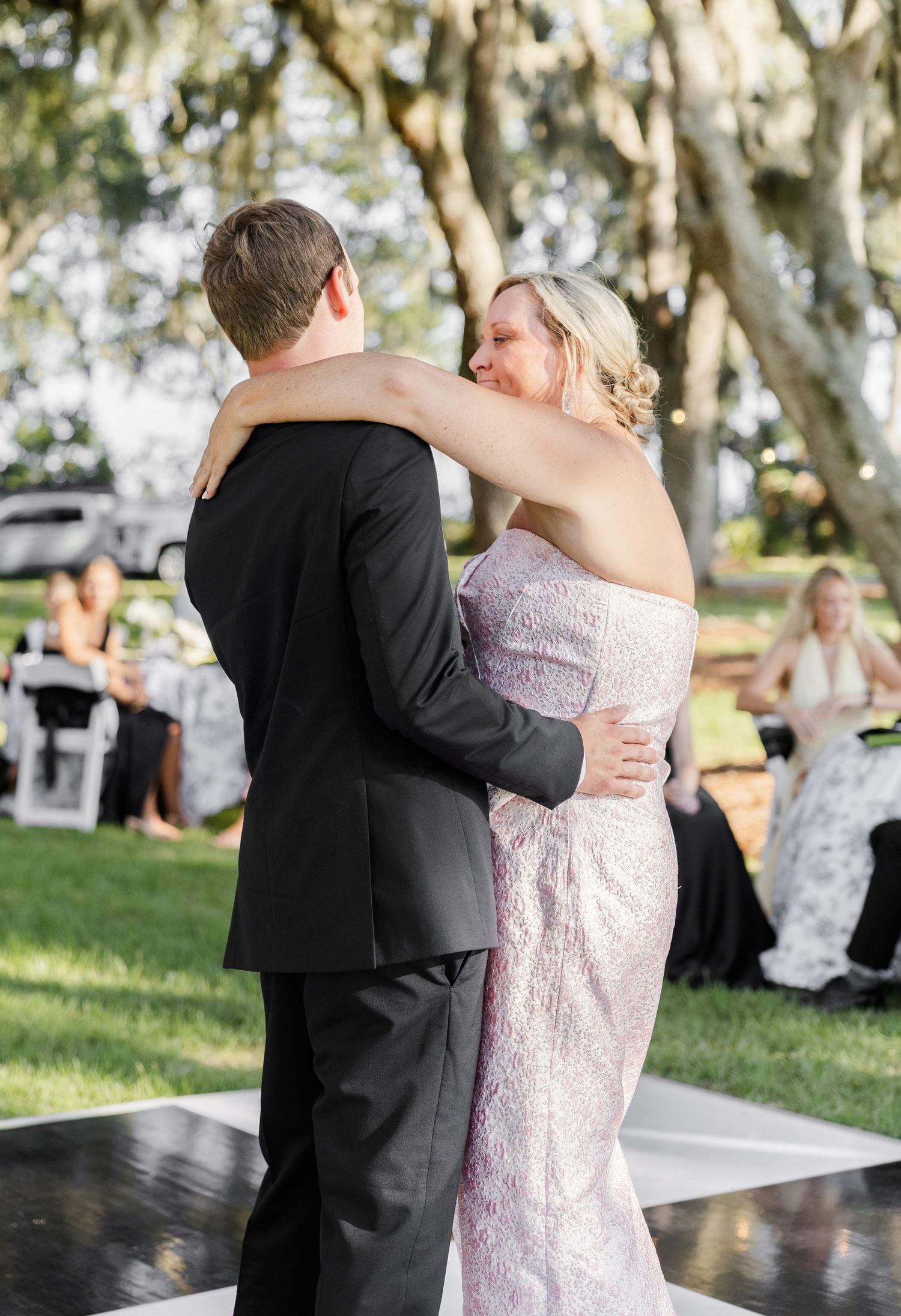Bride and groom share their first dance outdoors under oak trees at an elegant wedding reception.