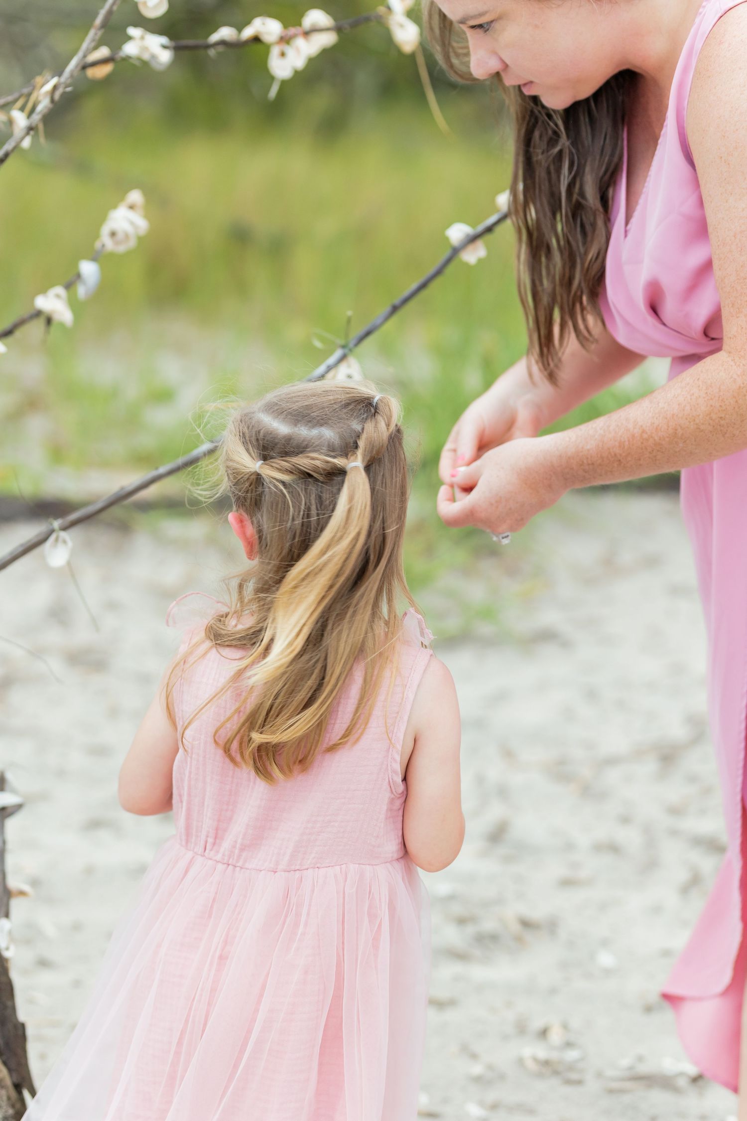 A young girl in a pink dress explores nature while looking at something hidden in the grass at sunset.