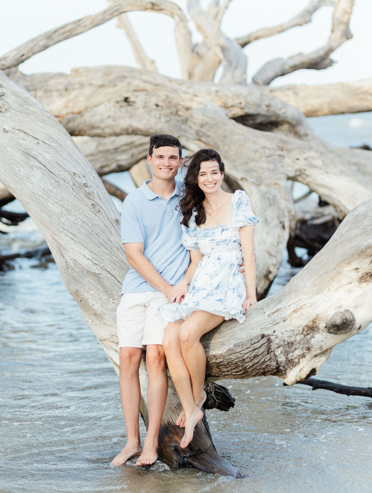 Romantic couple sitting together on driftwood by the ocean shore.