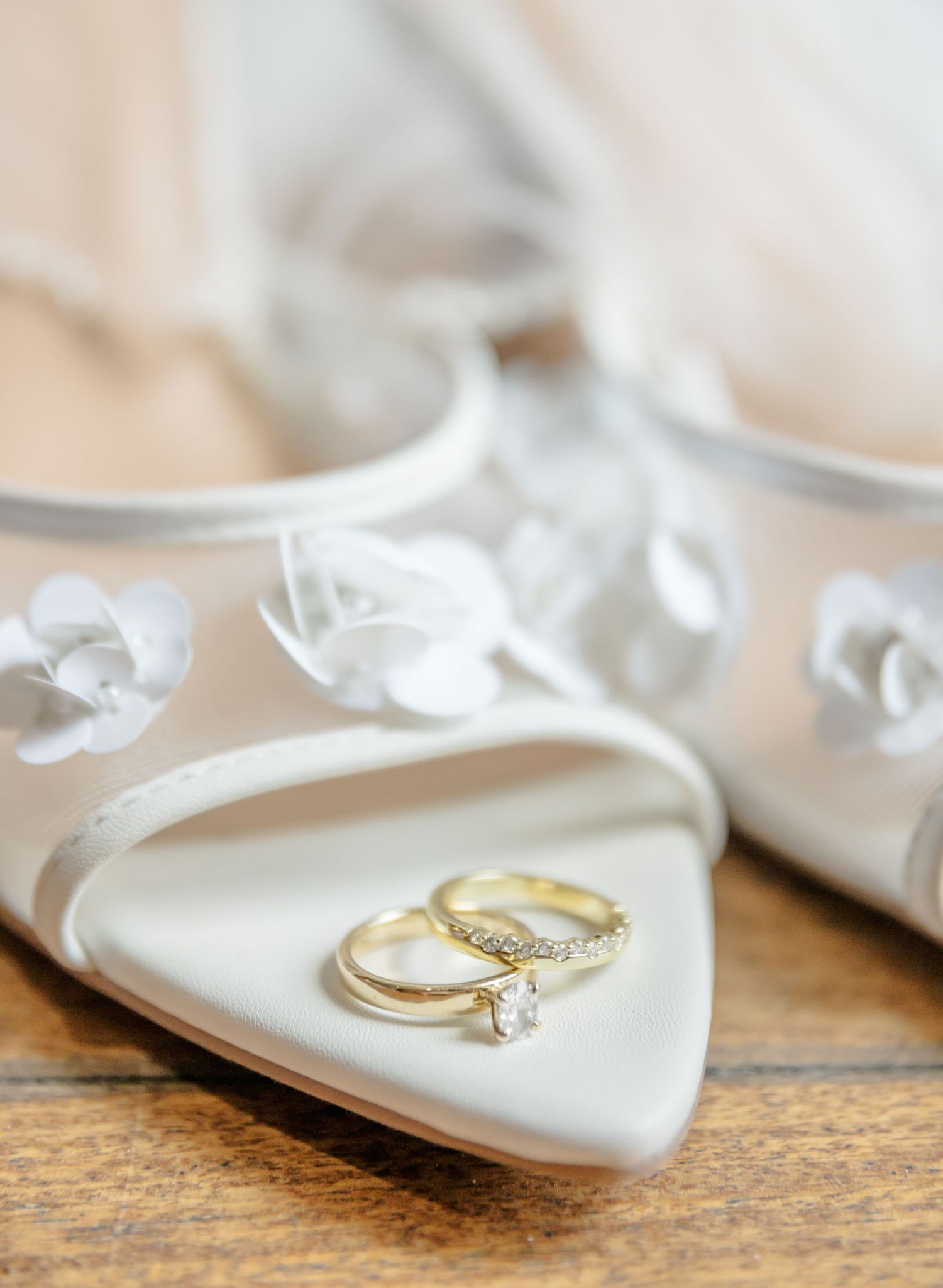 A delicate gold engagement ring rests on a white silk ribbon against a rustic wooden surface.