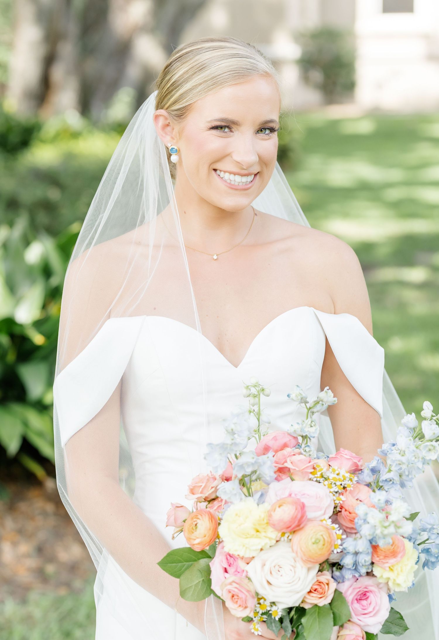 Bride holds beautiful pastel bouquet featuring coral, peach and blue flowers.