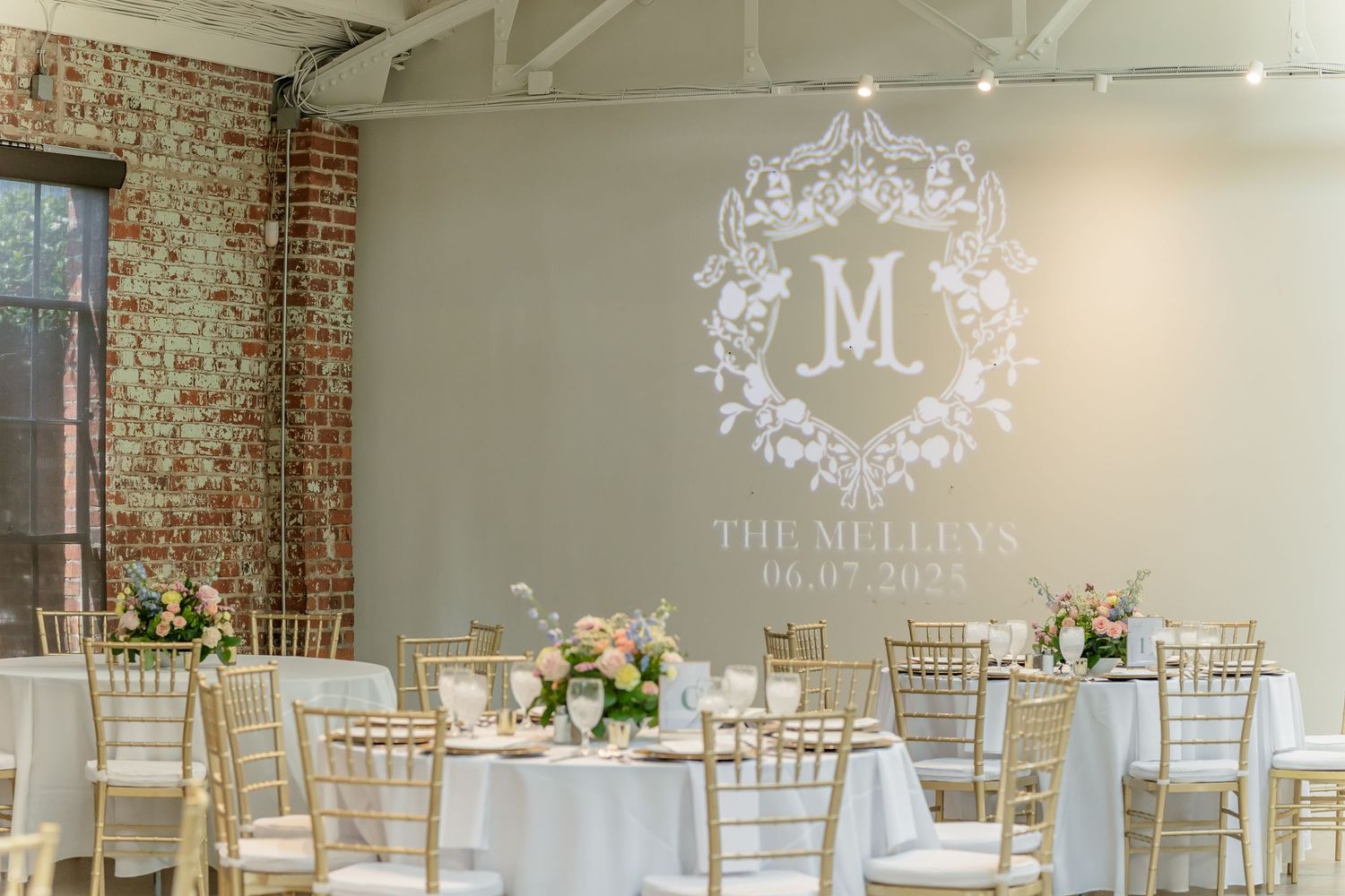An elegant wedding reception venue with monogrammed wall projection and gold chiavari chairs.