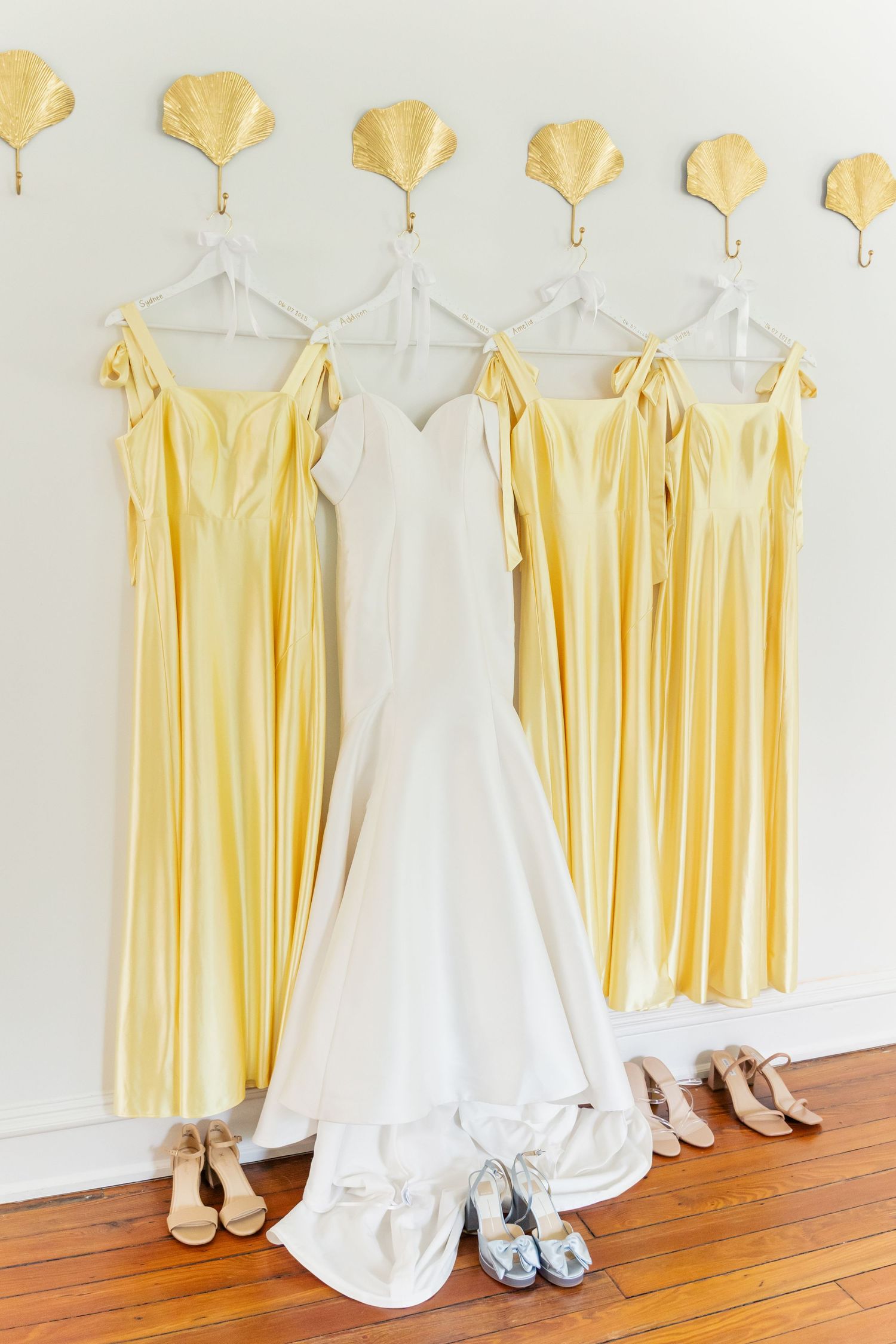 Yellow bridesmaid dresses and a white wedding gown hanging in a row on wooden hangers.