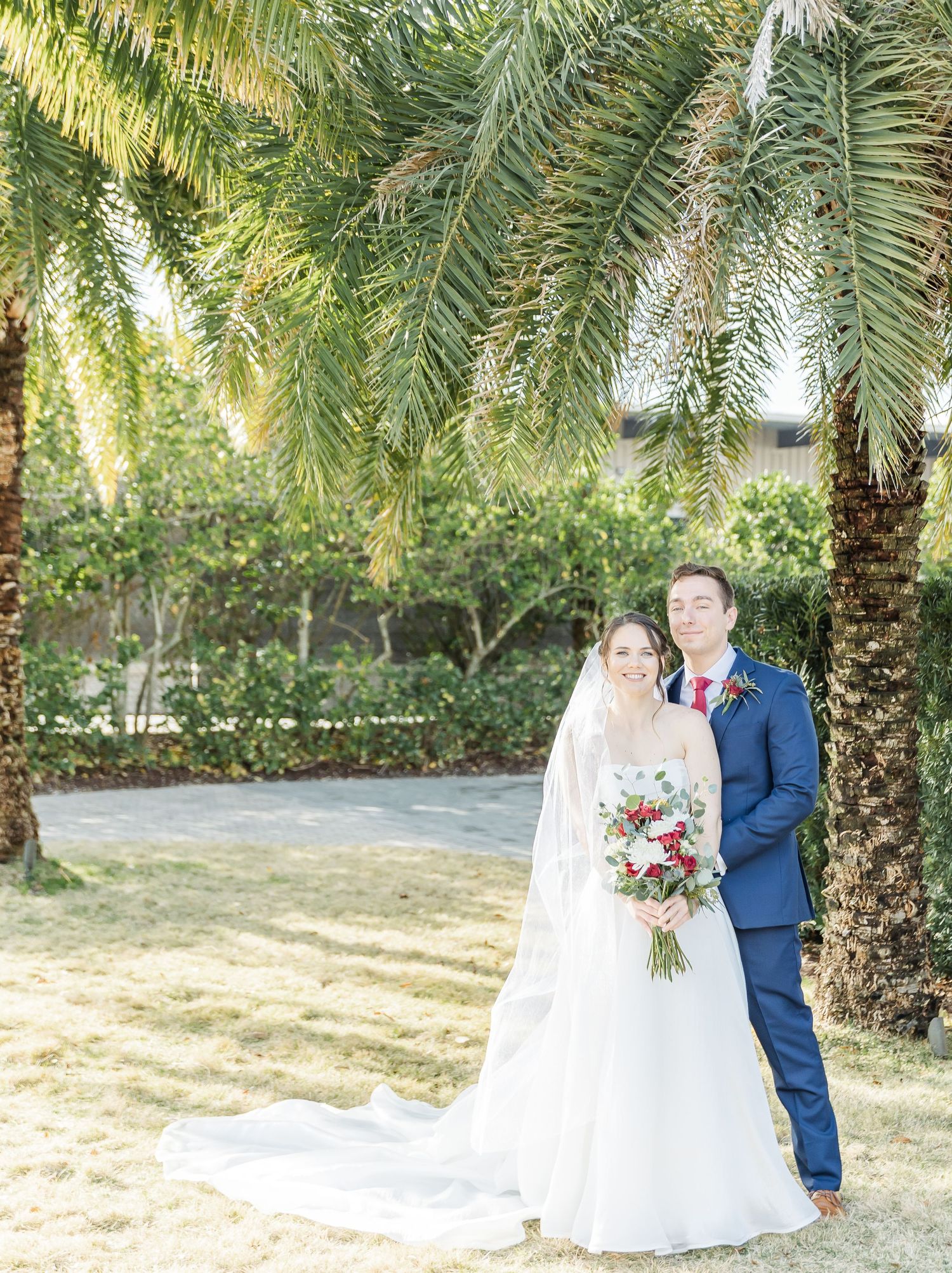 Wedding couple poses under palm trees in a garden with beautiful natural lighting.