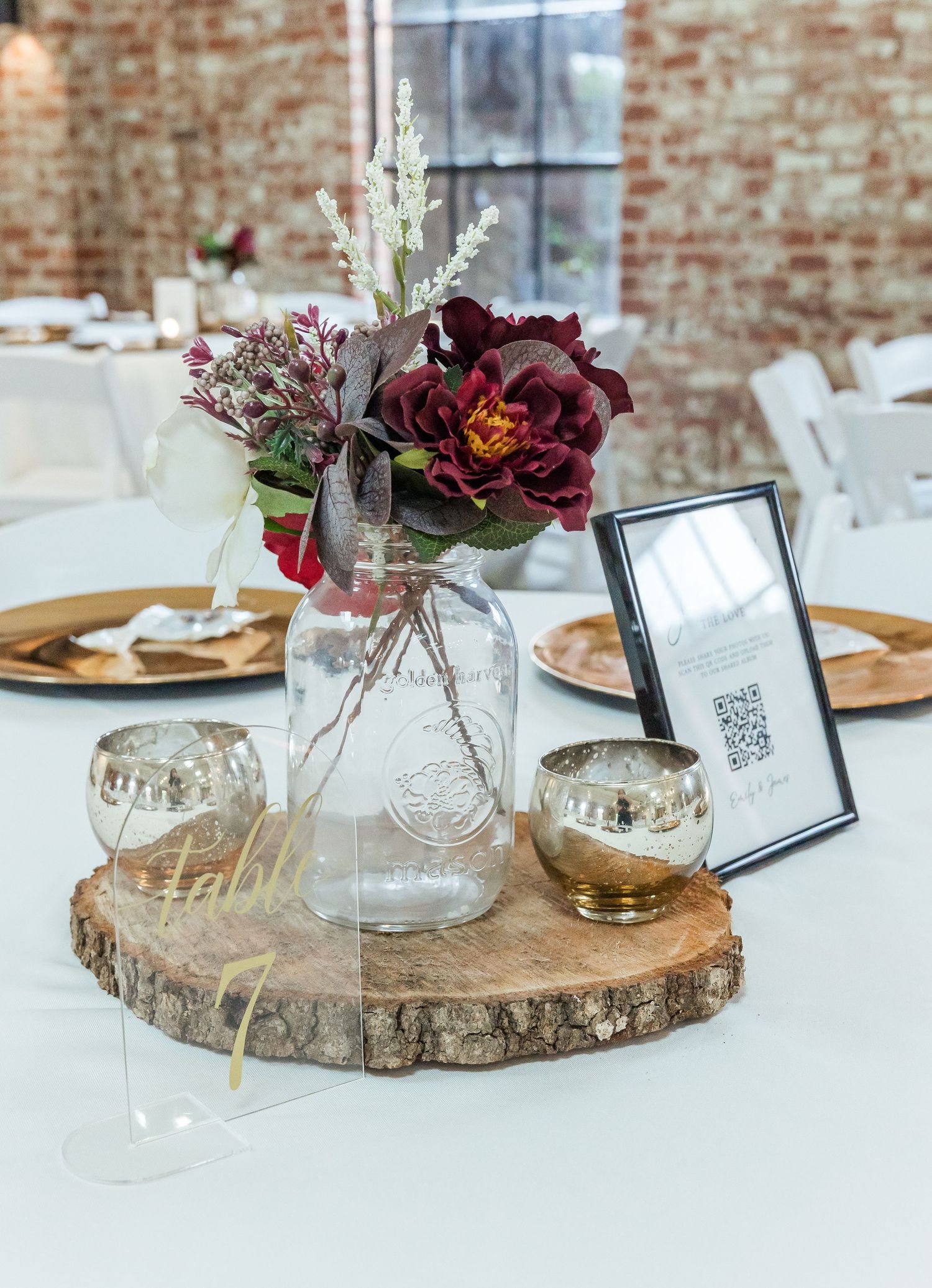 Rustic wedding centerpiece with burgundy flowers on wood slice charger and gold accents.