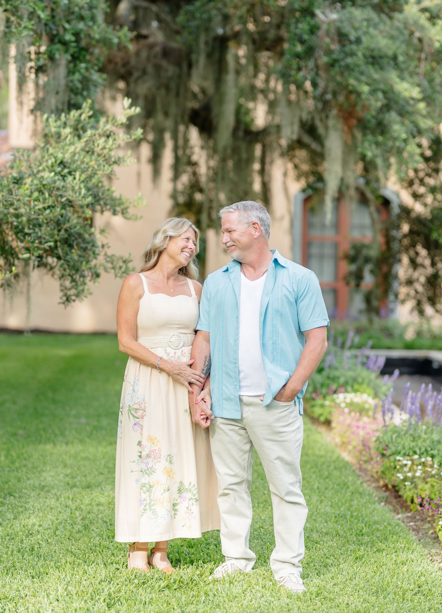 Couple walking hand in hand through a lush garden setting on a sunny afternoon.