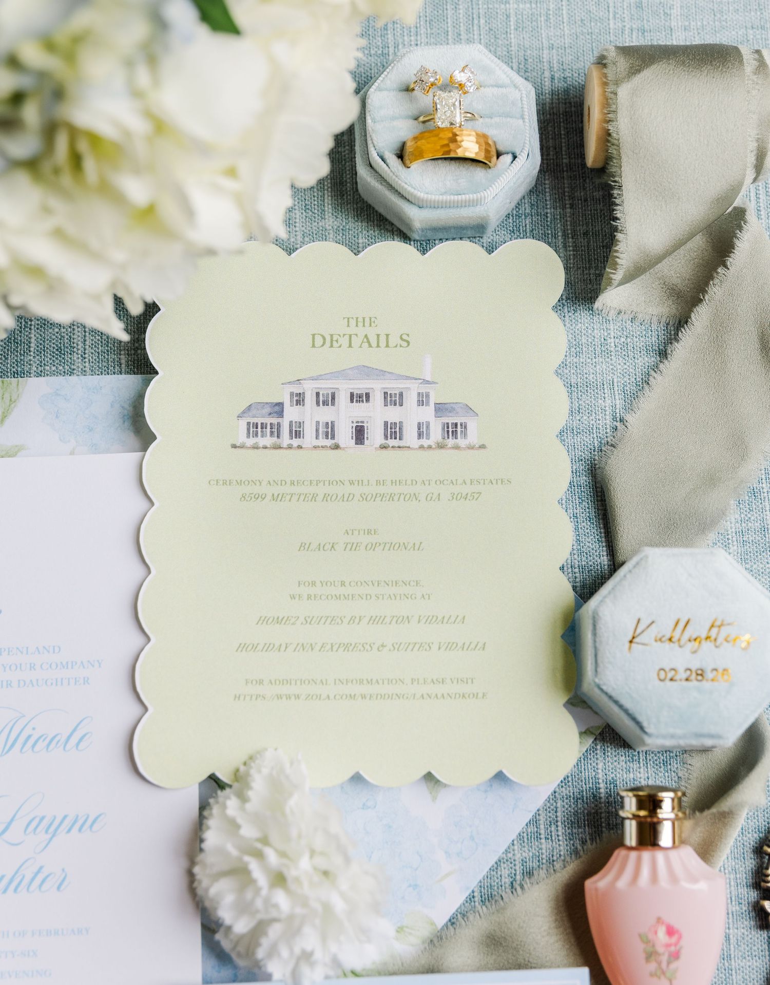 Elegant white wedding invitation suite with delicate floral details and soft blue calligraphy text on a textured surface.