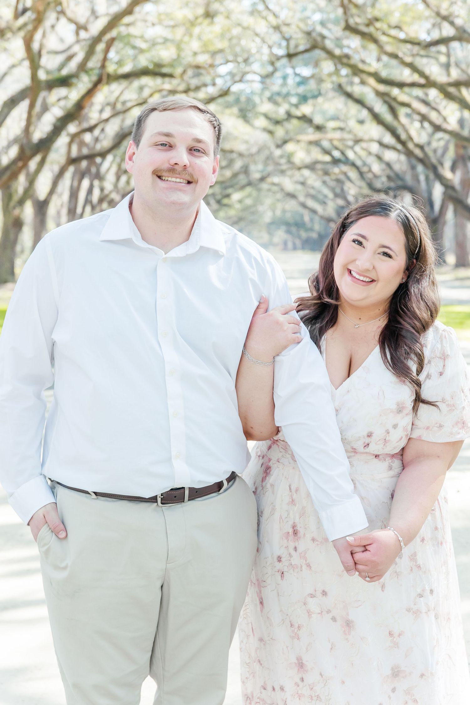 Couple poses for engagement photos on a tree-lined path in spring.