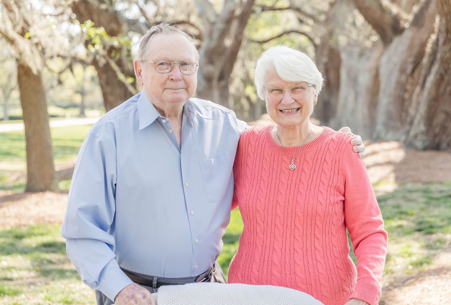 Elderly couple in casual attire smiling together in scenic park setting.