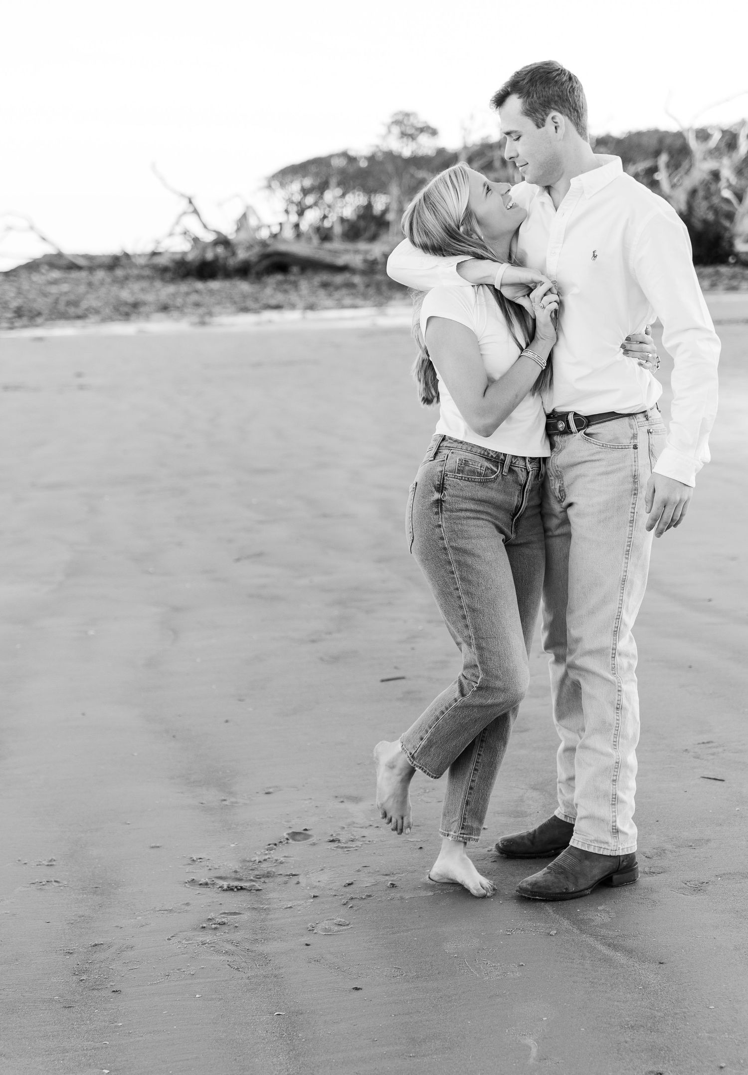 A black and white photo of a couple sharing an intimate moment on the beach.
