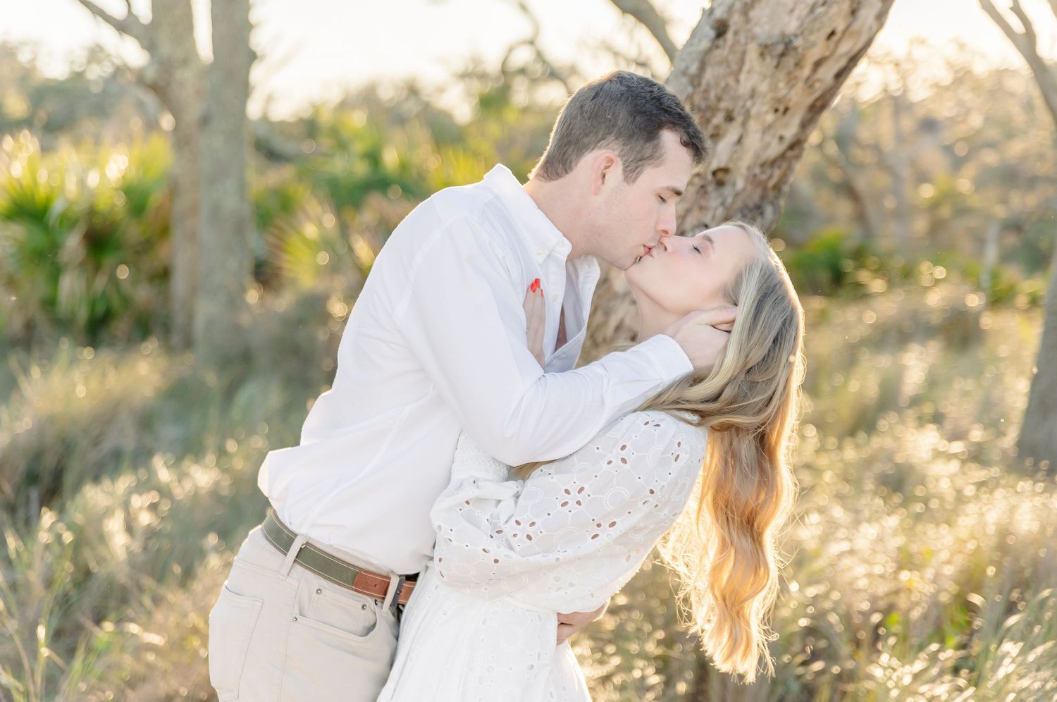 A loving couple shares a romantic kiss in a sunlit natural setting.