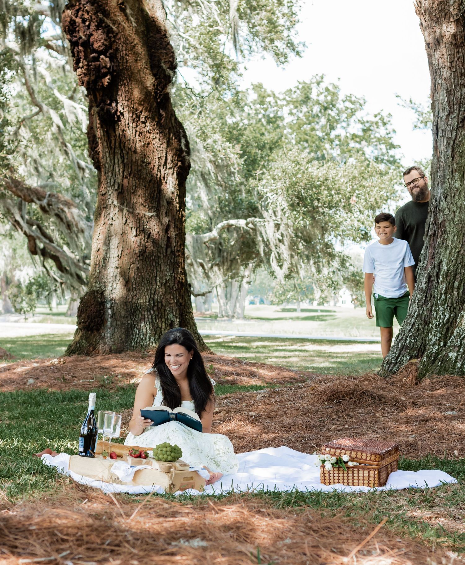 Family having a picnic under ancient oak trees while playing hide and seek.