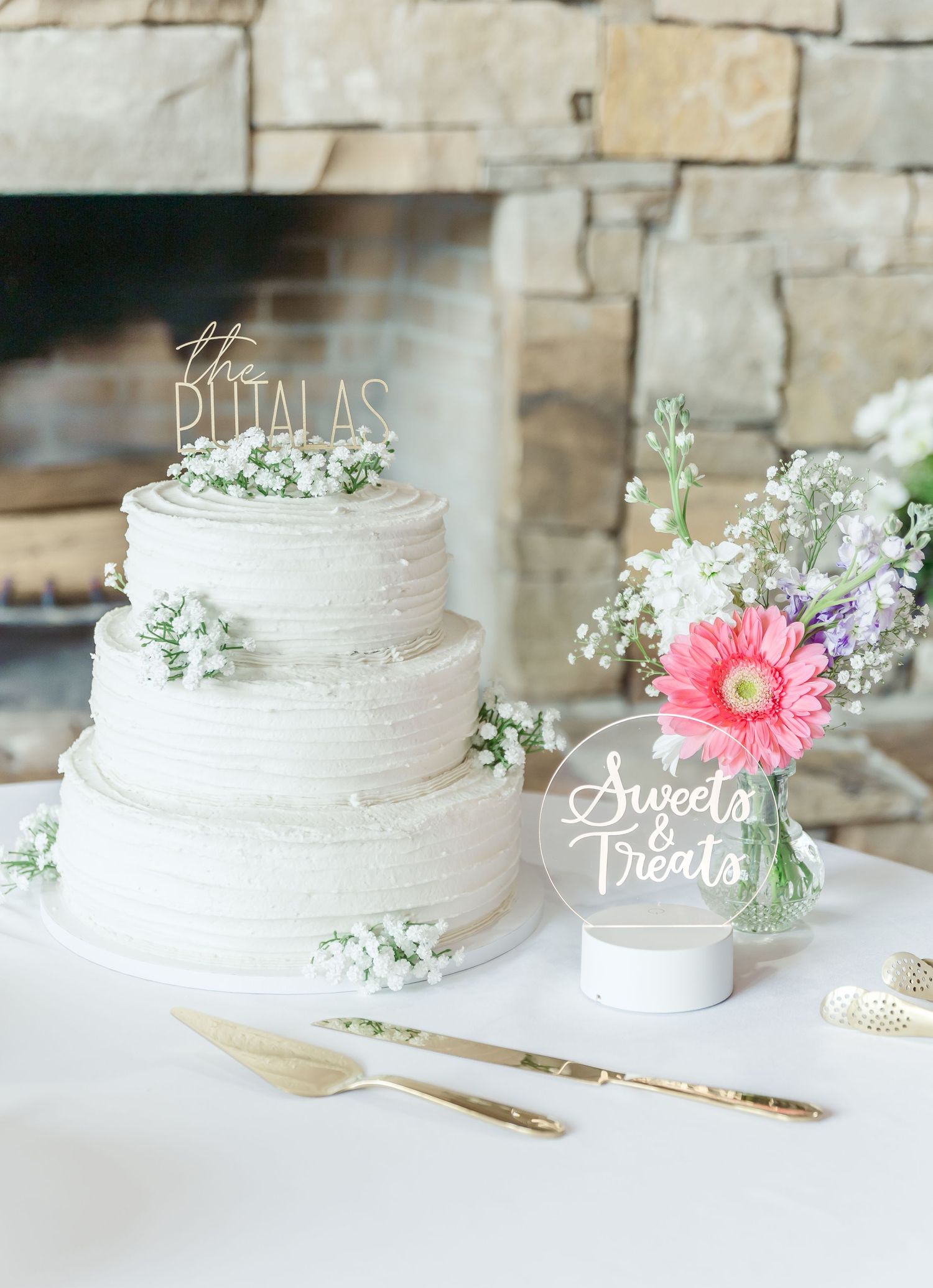 White tiered wedding cake decorated with baby's breath and pink gerbera daisies.