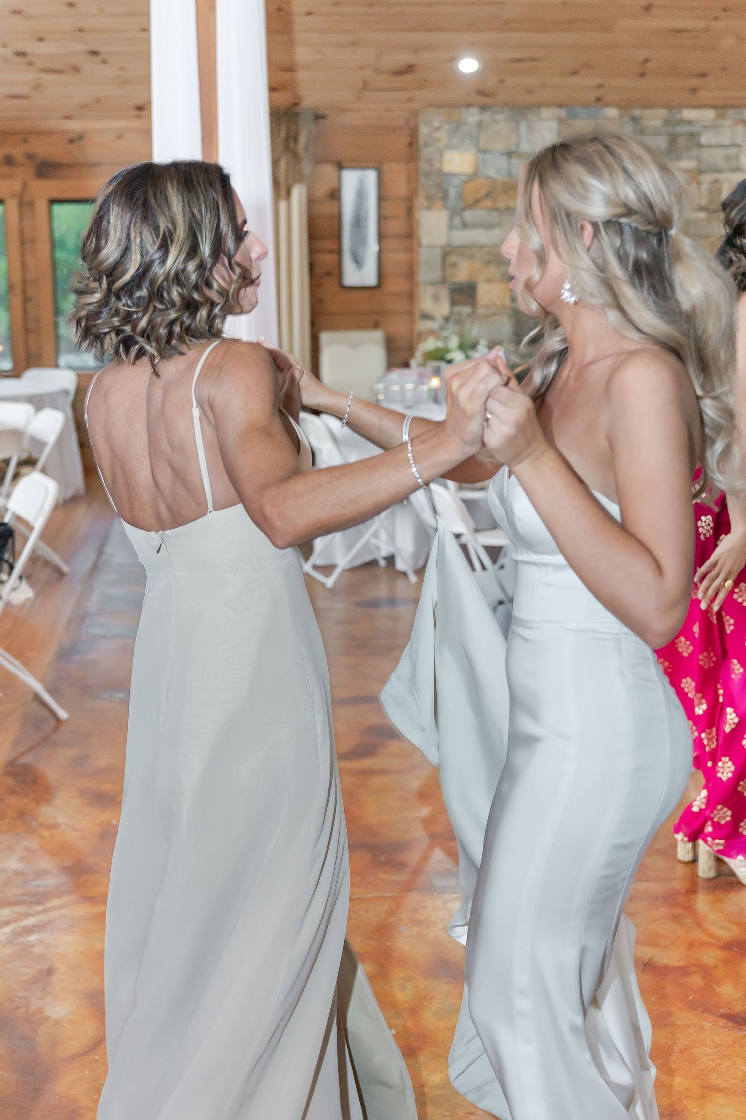Two people in elegant silver dresses dancing together at a rustic wedding reception.