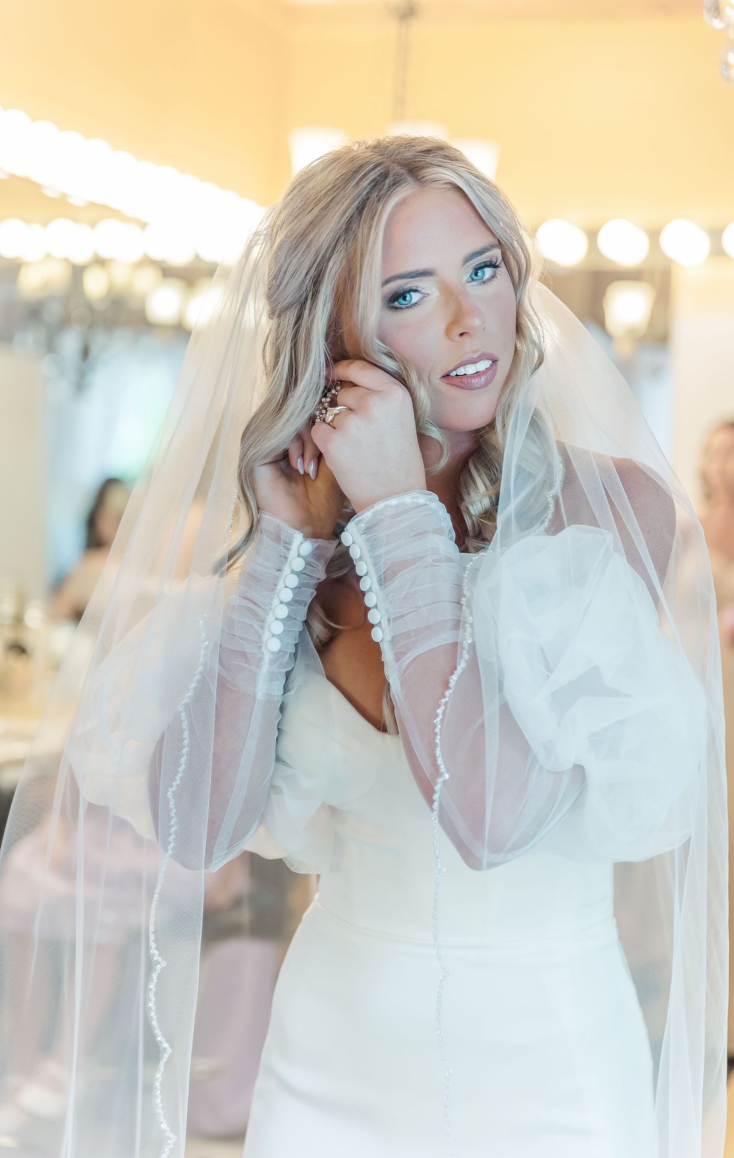 Ethereal bridal portrait showing a stunning white wedding gown with sheer sleeves and flowing veil.