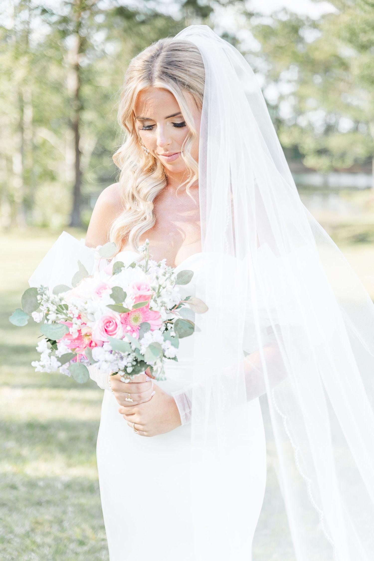 Ethereal bridal portrait with soft lighting showcasing veil and pink floral bouquet.