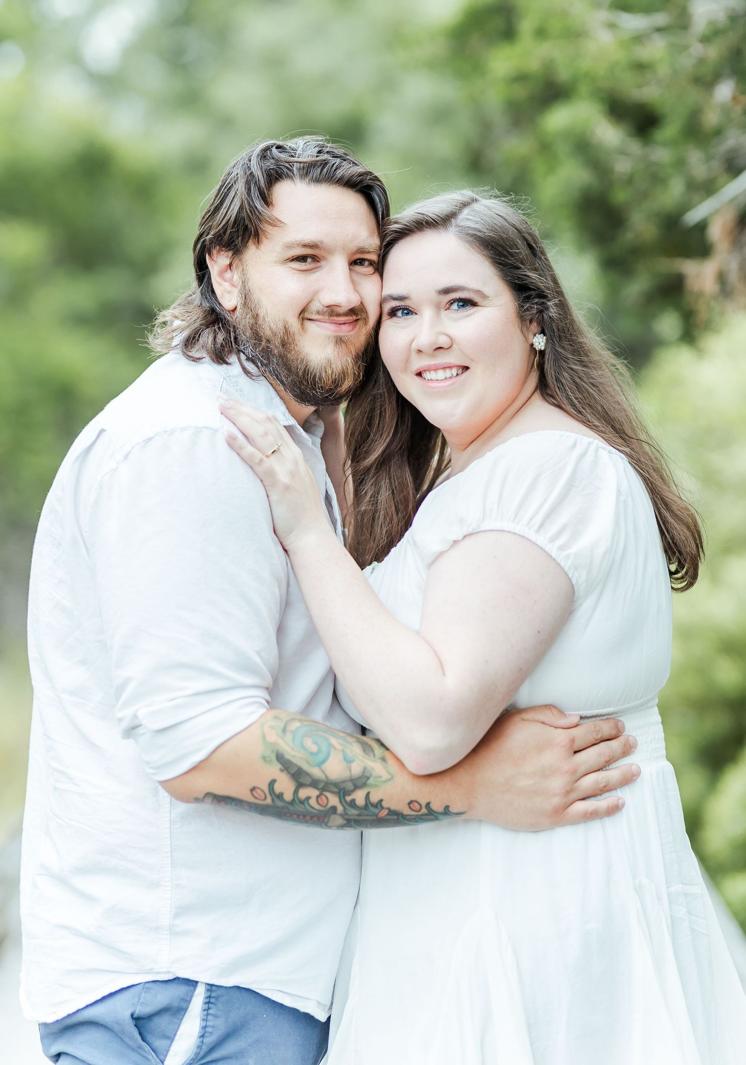 Happy couple in coordinating white outfits embrace outdoors in a natural setting.