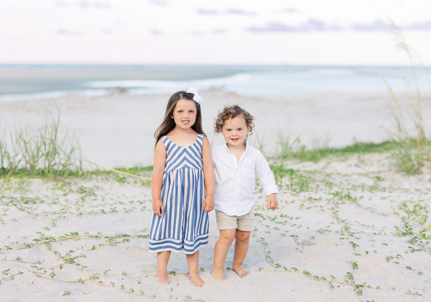 Two people in matching blue and white striped outfits walk together on a sandy beach during a photoshoot.