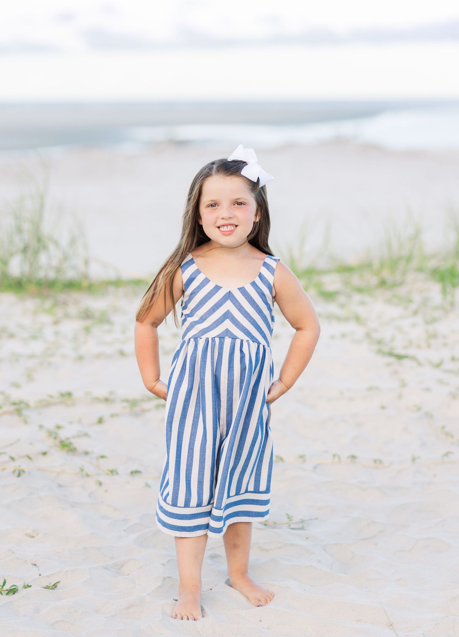 Young child in a blue and white striped dress playing on a sunny beach.