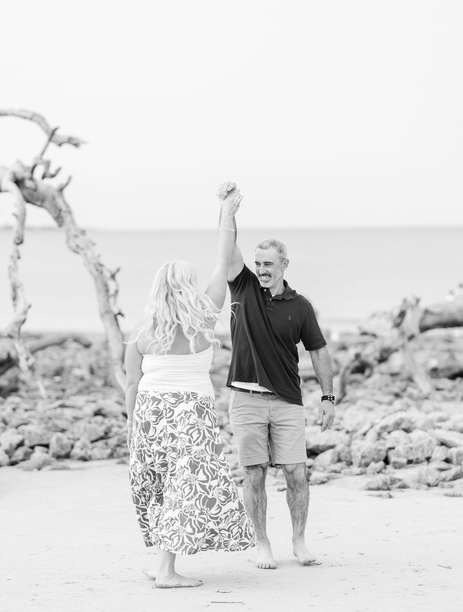 A joyful moment captured in black and white as a couple celebrate on a rocky beach with their hands raised.