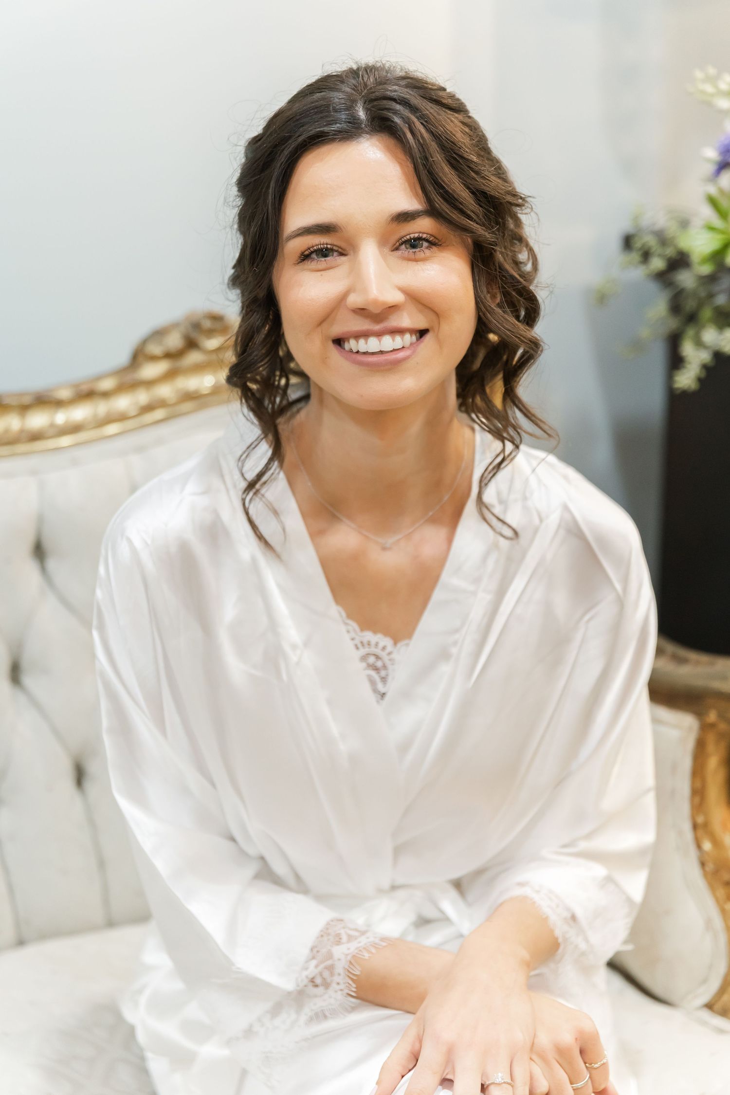 A person in a white silk robe sits on an elegant couch while getting ready for a special occasion.