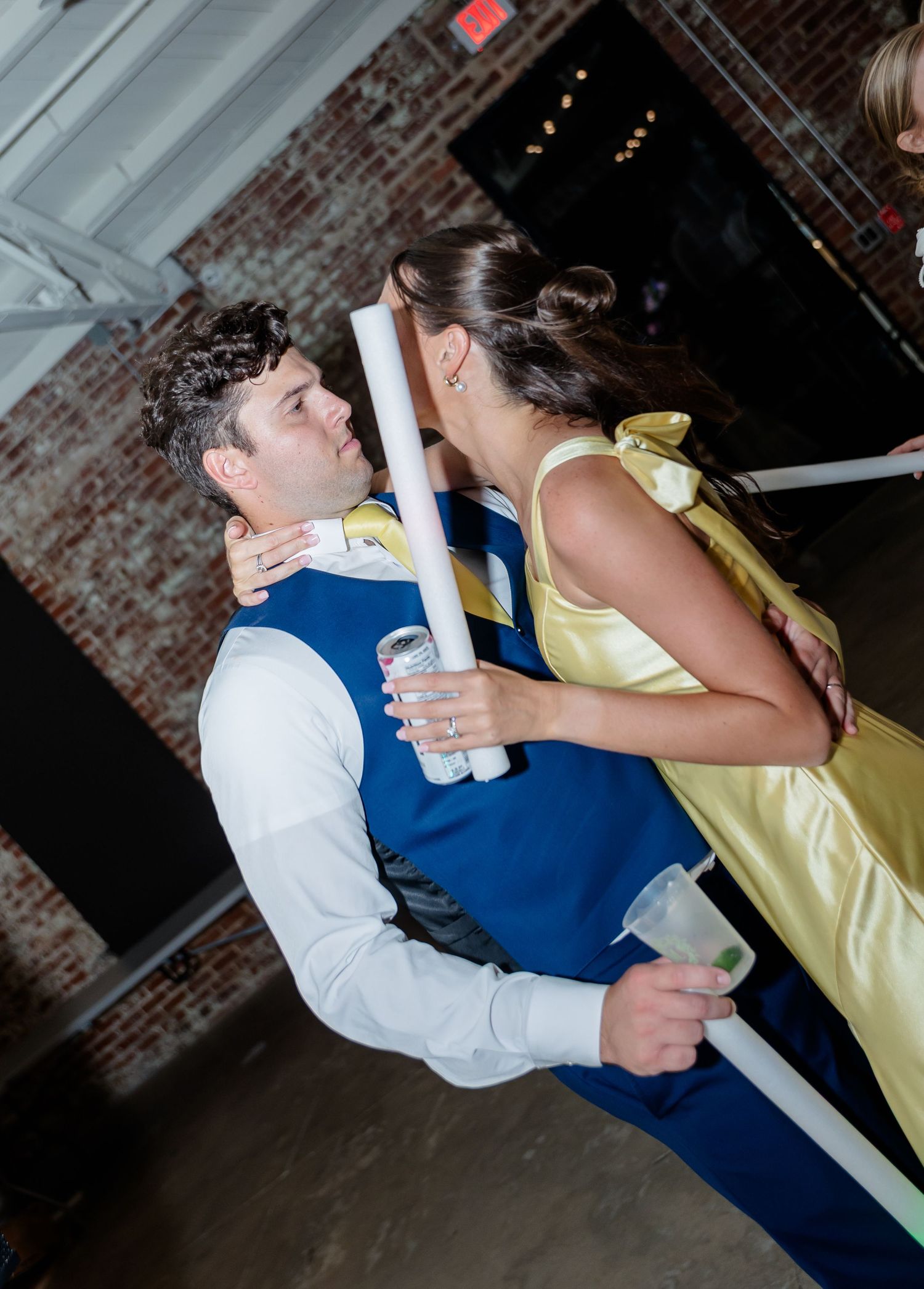 A couple in formal attire dancing together at a wedding reception with brick walls in the background.