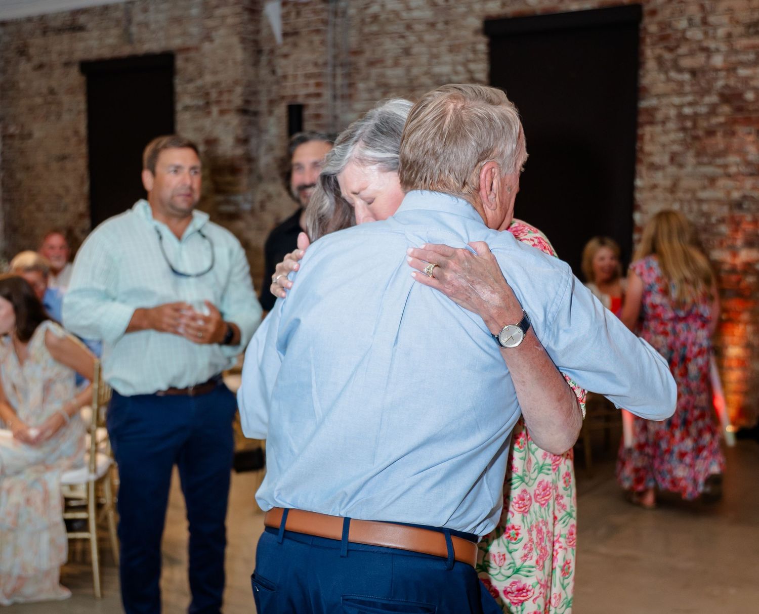 Couples slow dancing together in a rustic brick-walled venue during an evening celebration.