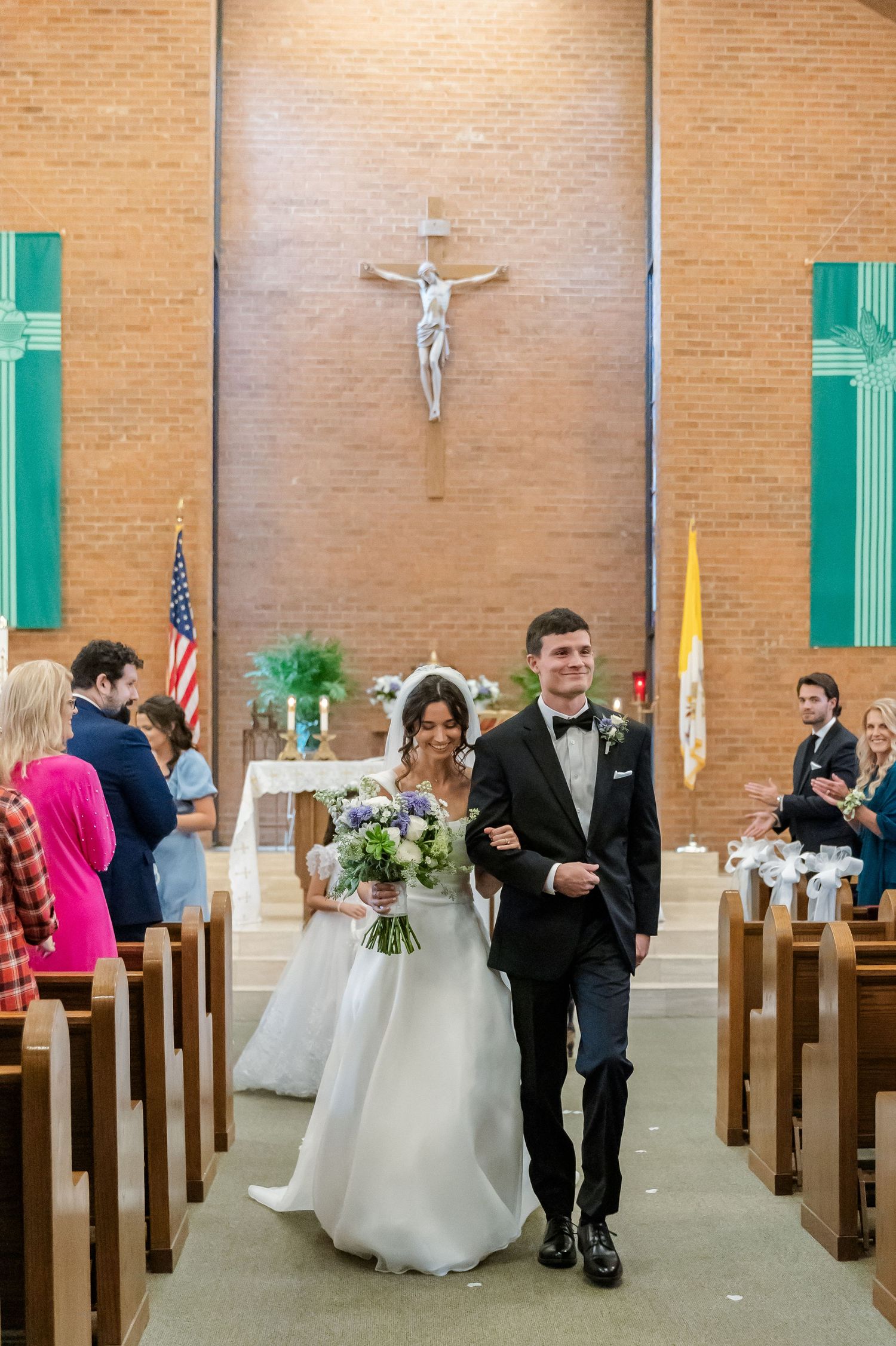 A traditional Catholic church wedding ceremony with wooden pews and brick walls decorated with green accents.