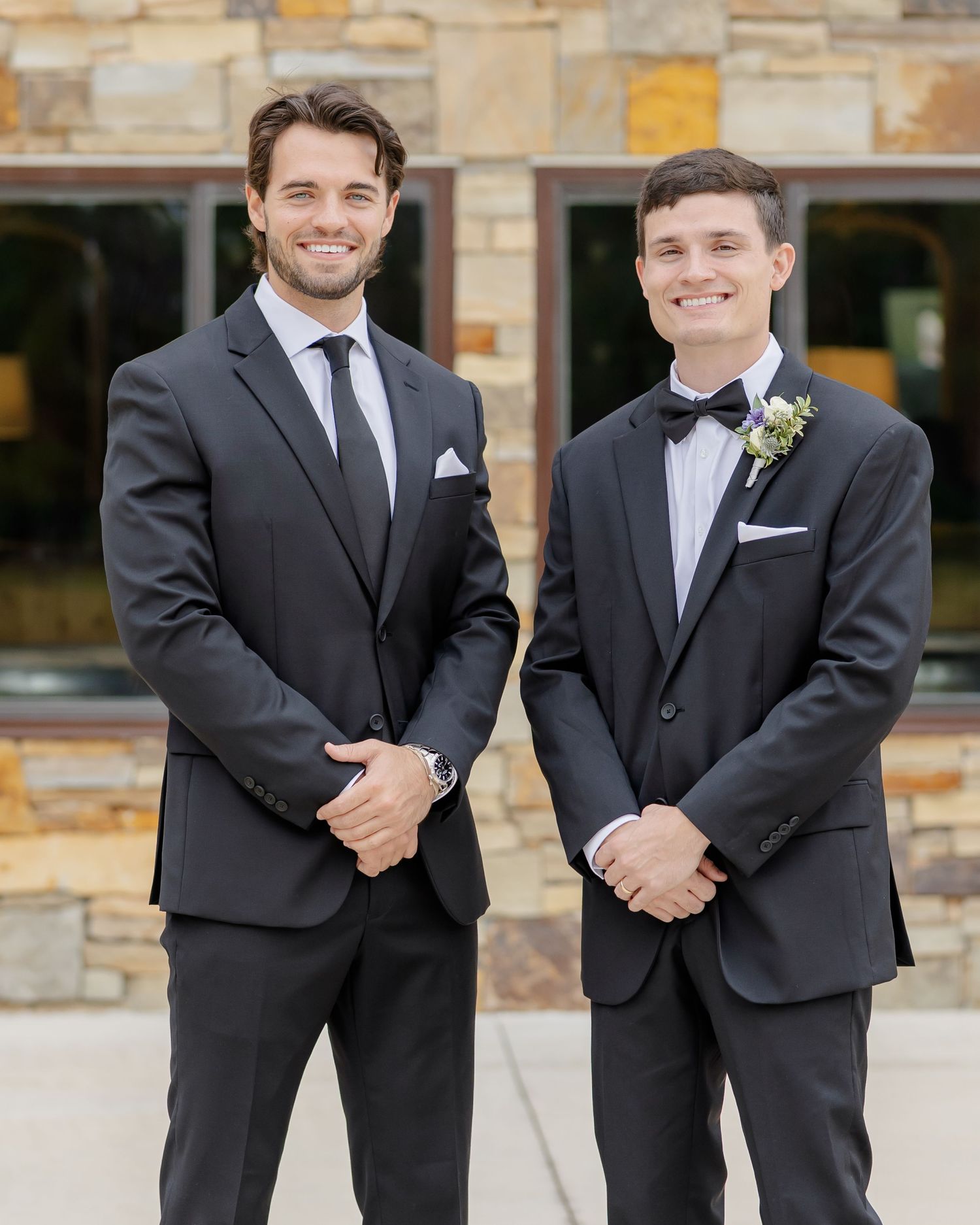Groomsmen in matching black suits and ties share candid laughs and smiles while posing together outdoors.