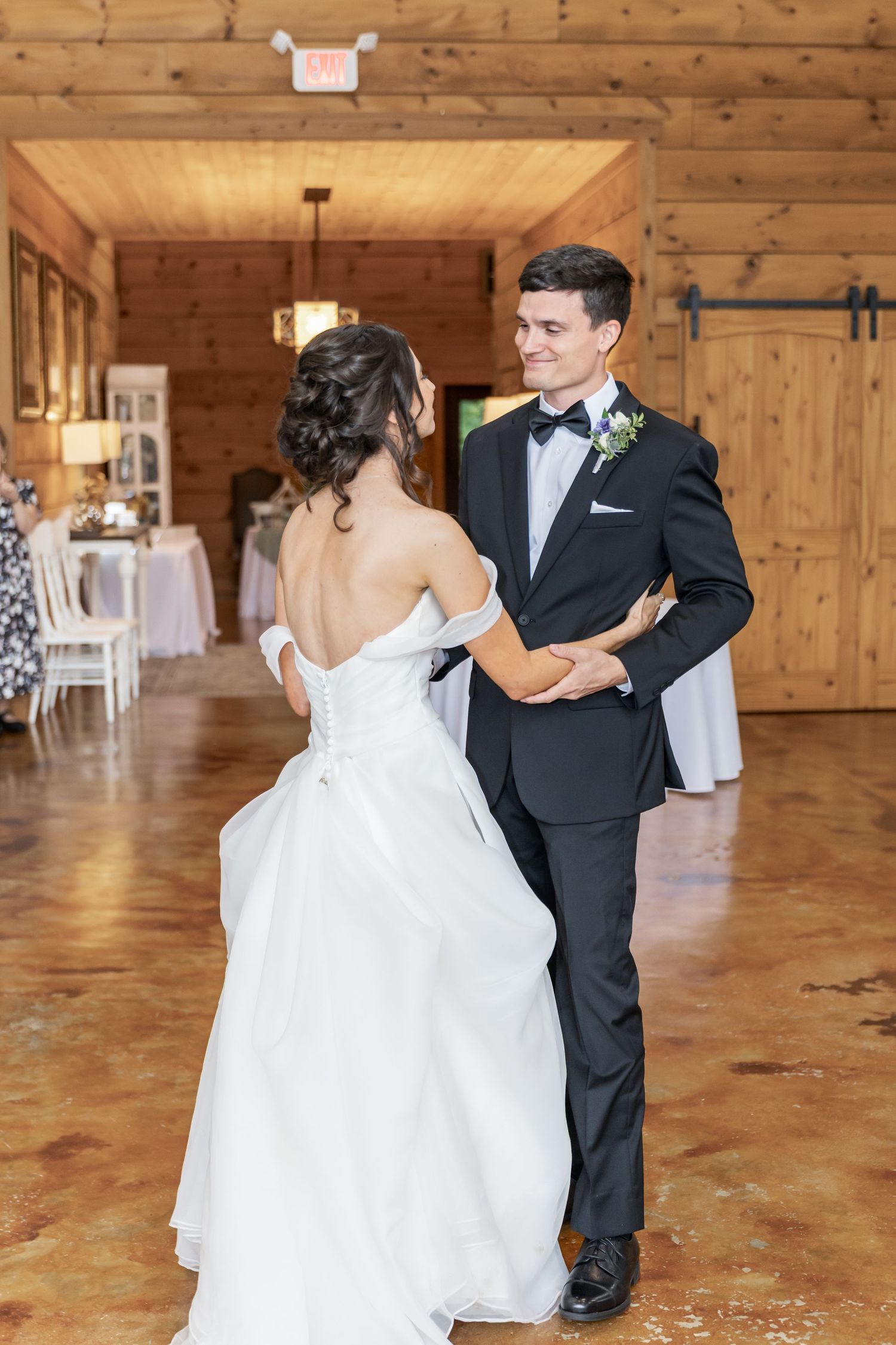 Newlyweds dance together on a wooden floor in a rustic barn reception venue with elegant decor.