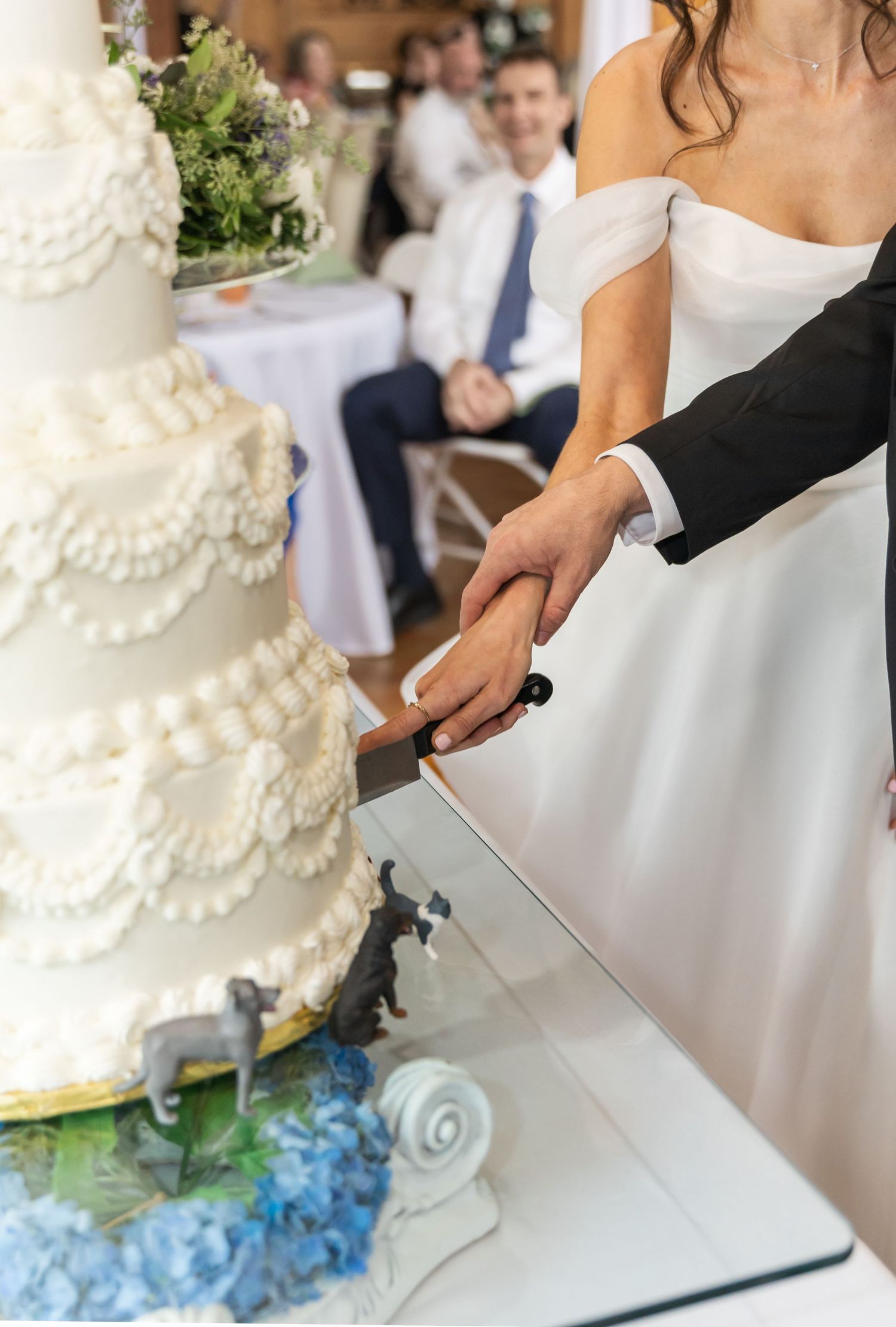Couple cutting their elegant white tiered wedding cake with delicate lace details and blue accents at their reception.
